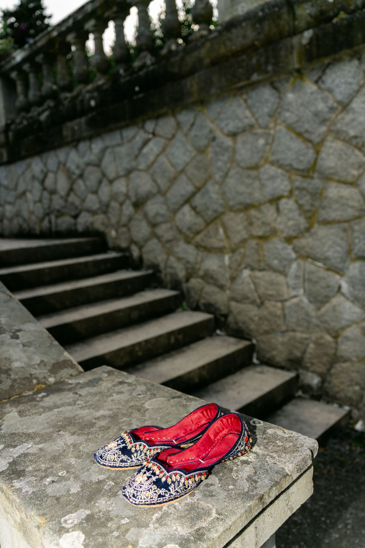 Red embellished bridal shoes displayed on stone steps with vintage aesthetic.