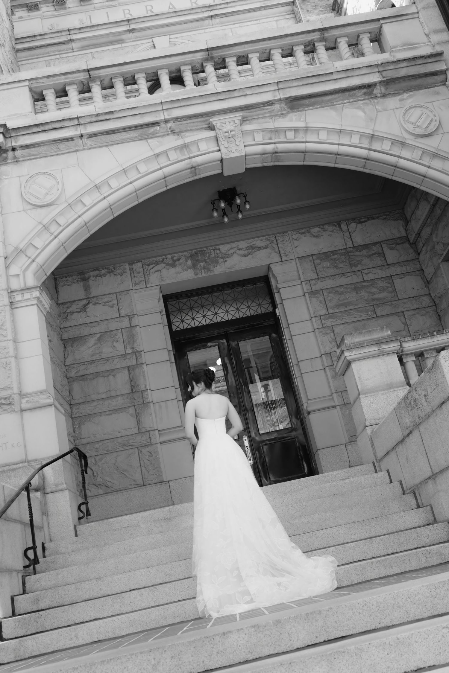 Black and white sequence of bride ascending stone stairs at historic building entrance.