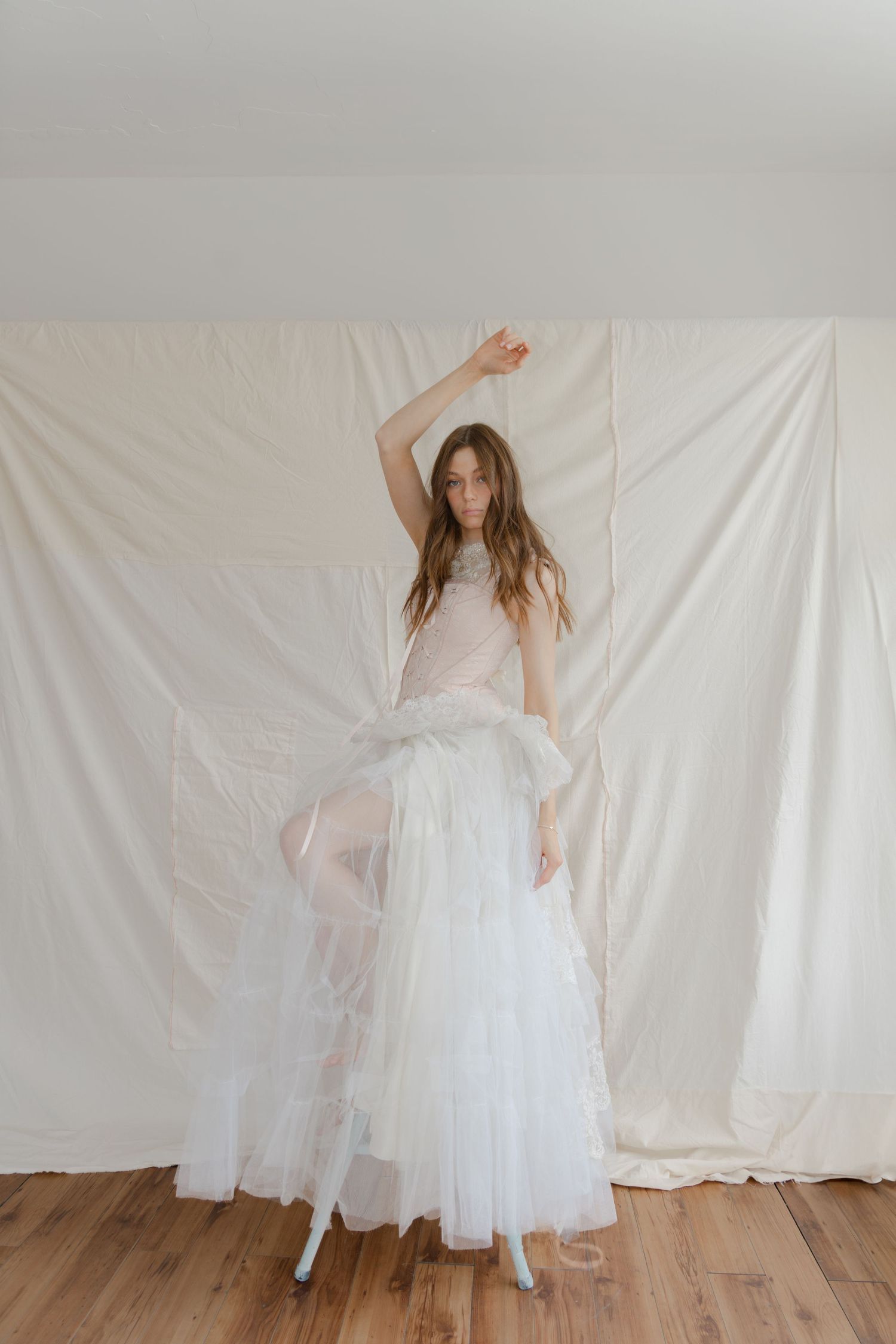 Young model in flowing white dress poses gracefully against white backdrop in ethereal dance-inspired photoshoot series.