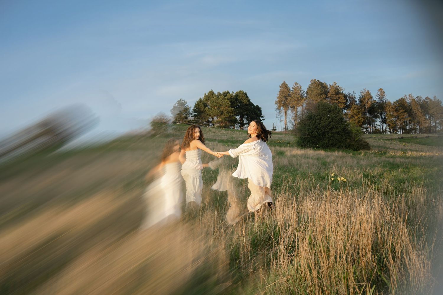A blurred motion shot of a couple dancing in a field at sunset with trees in the background.