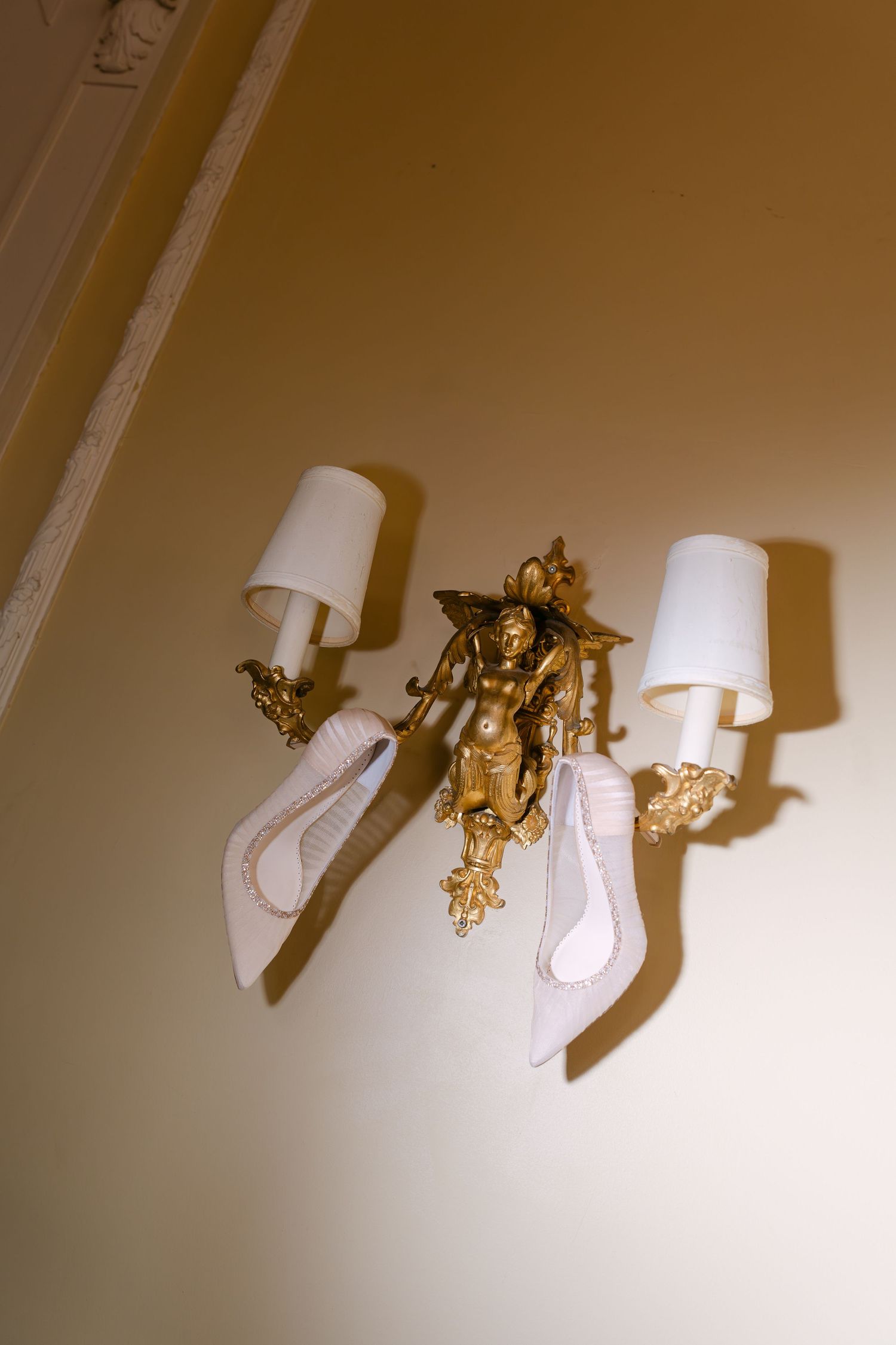 Ornate gold cherub wall sconce with white lampshades and draped ribbon in classic wedding venue.