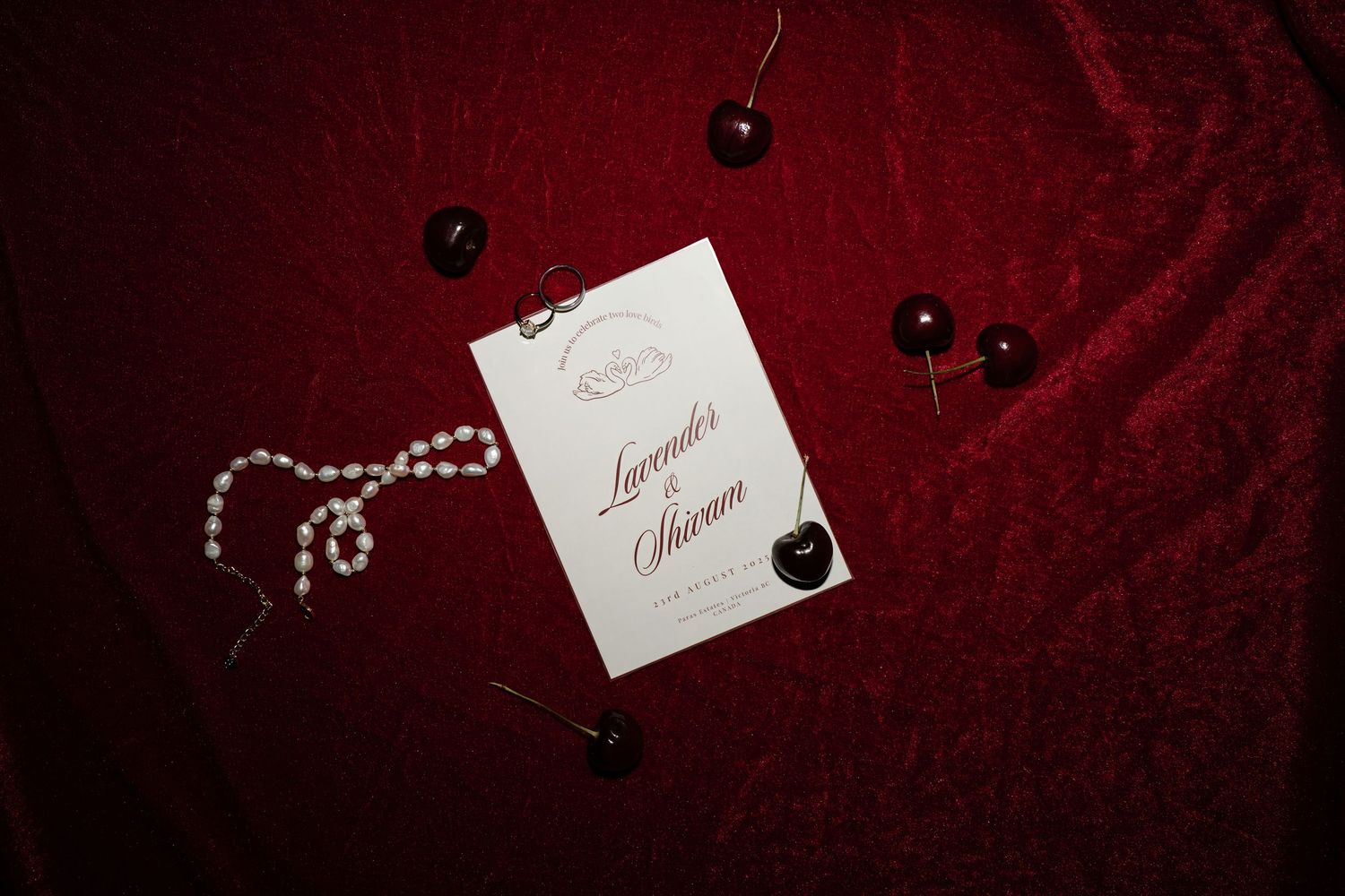 Elegant wedding invitation cards and decorative elements arranged on deep red velvet fabric with pearls and crystals.
