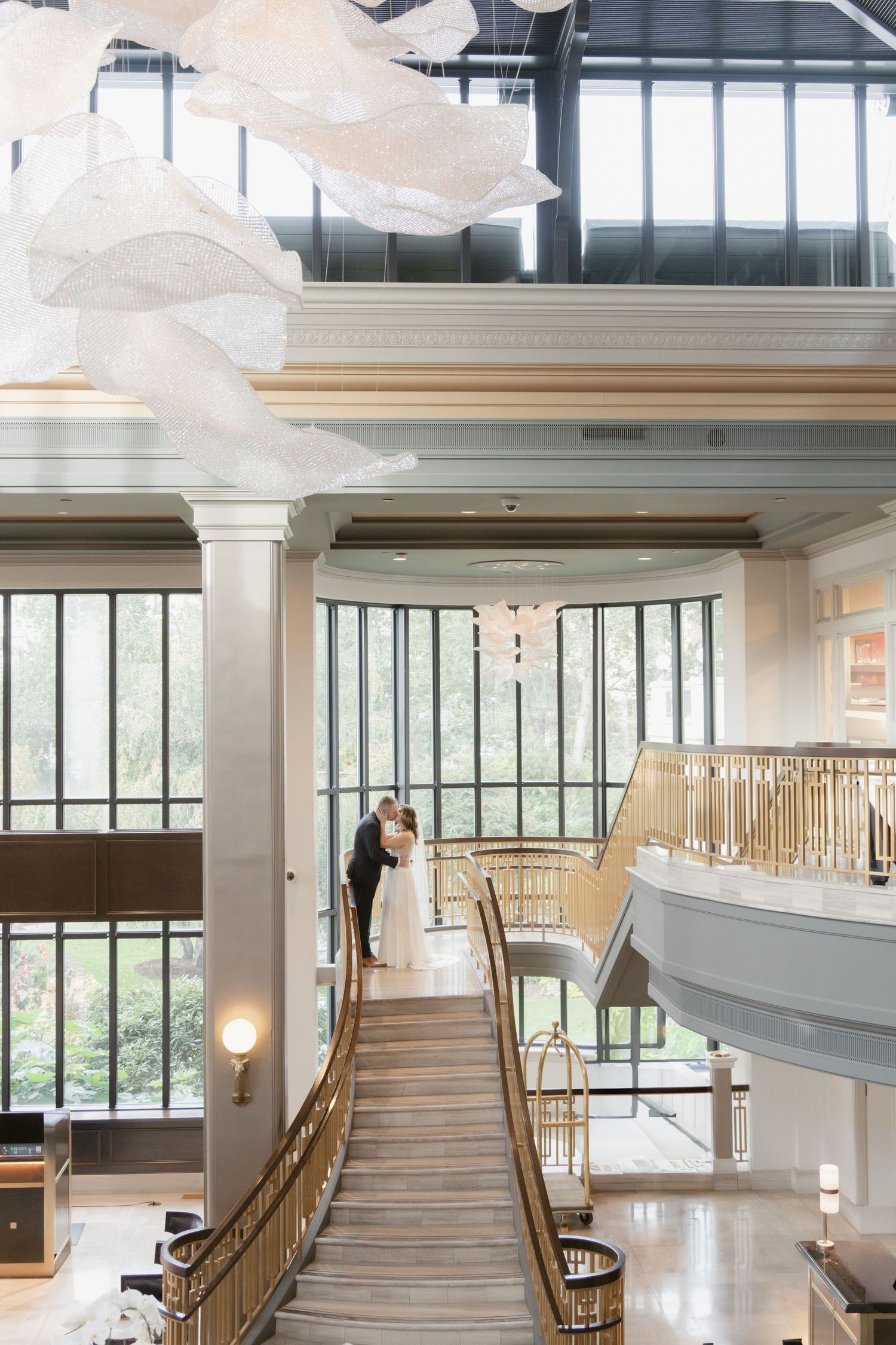 Elegant staircase with golden railings and large windows in modern wedding venue.