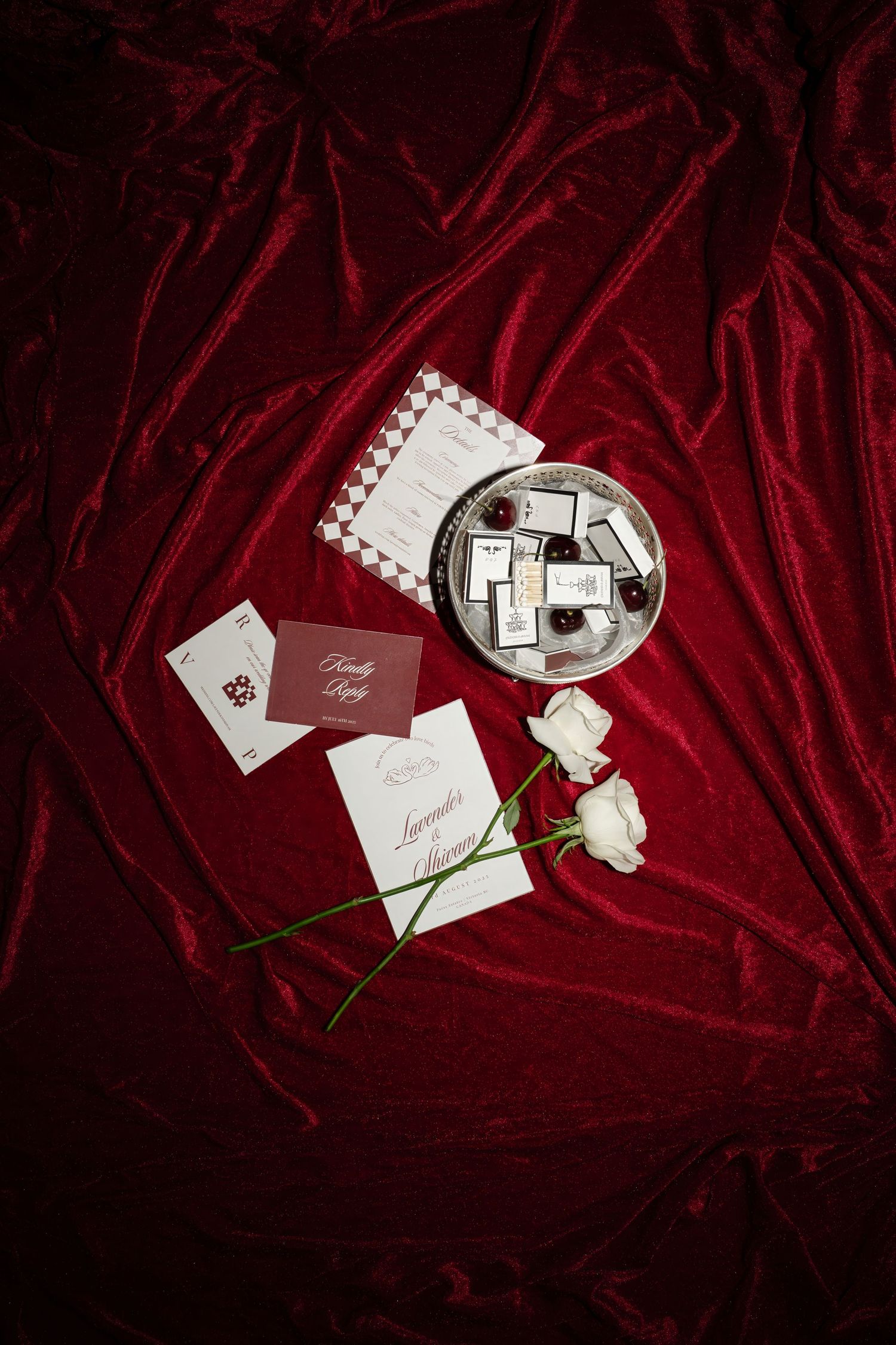 Wedding invitations and rings displayed on luxurious red velvet fabric with elegant lighting and shadows.
