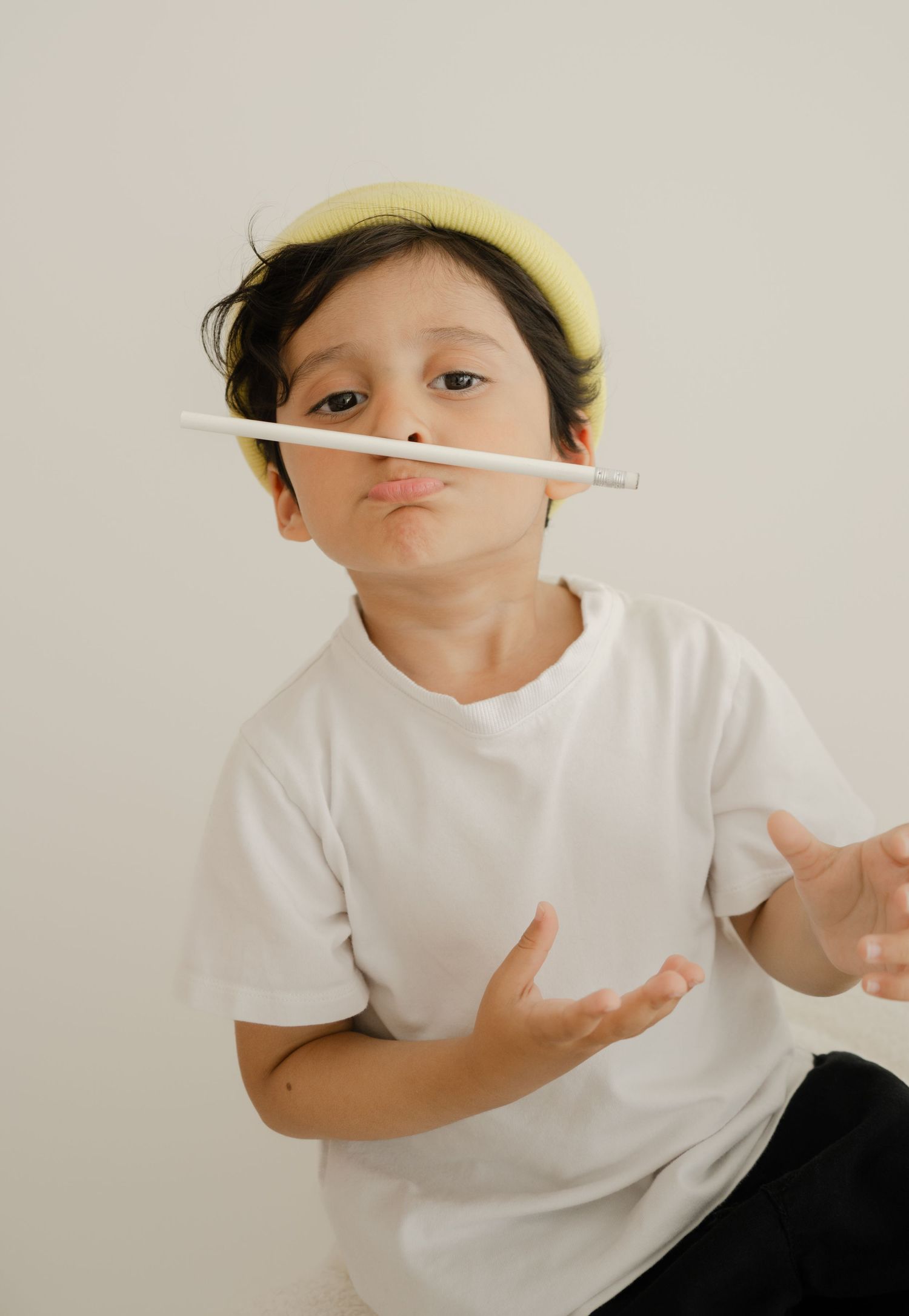 Playful portrait in white t-shirt and yellow beret balancing pencil.