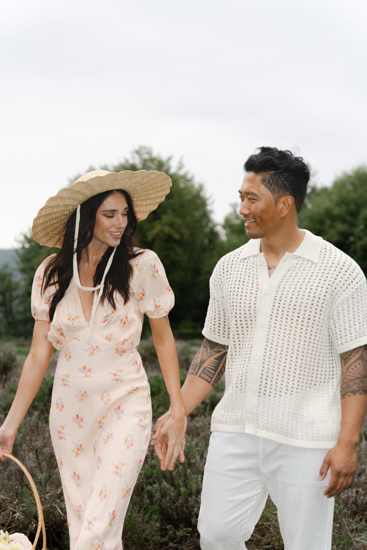 Couple in coordinated white outfits walking through flowering meadow in Abbotsford.