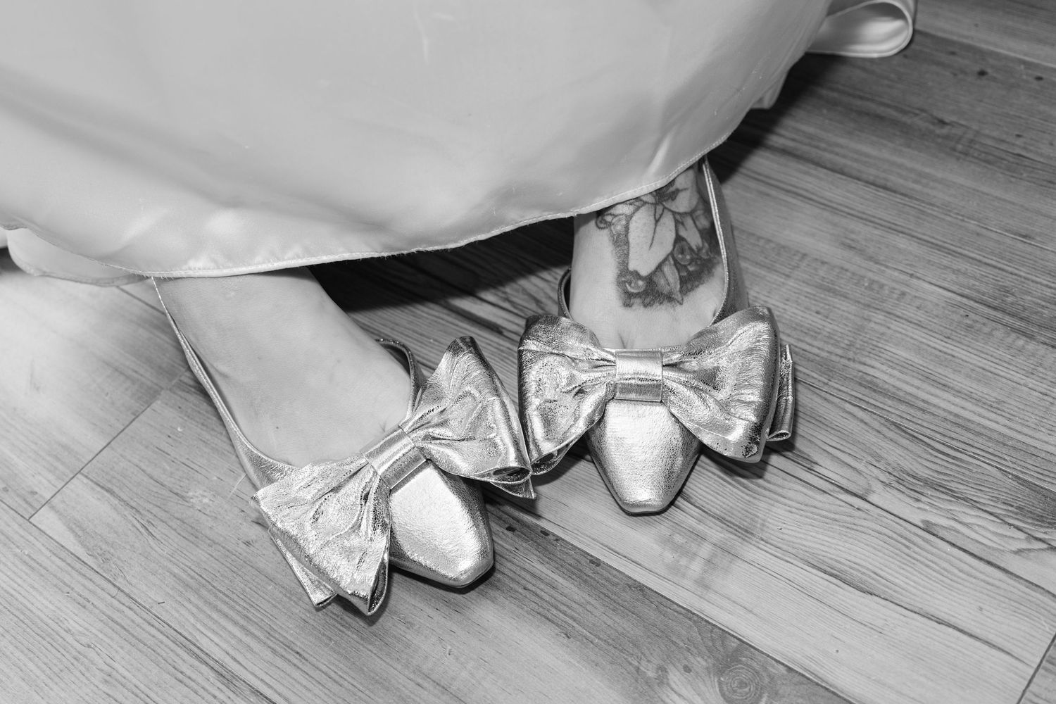 White bridal shoes and dress hem detail on hardwood floors at a wedding venue.