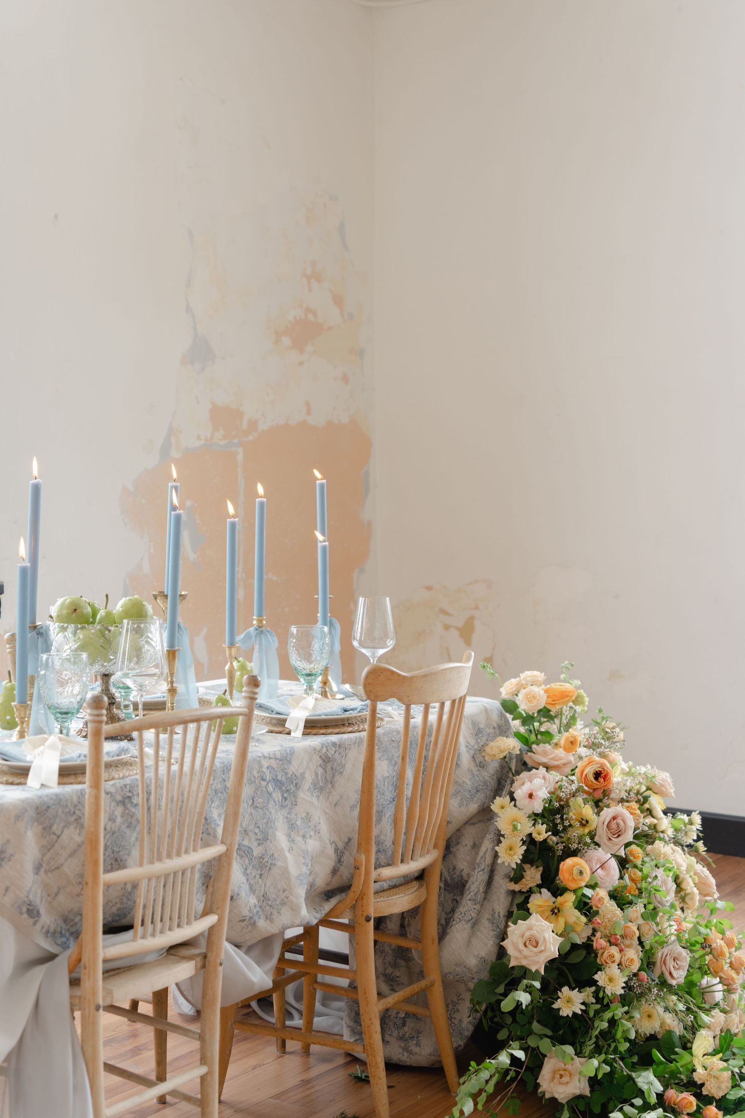 Wedding reception setup with blue taper candles and floral arrangements on wooden chairs.
