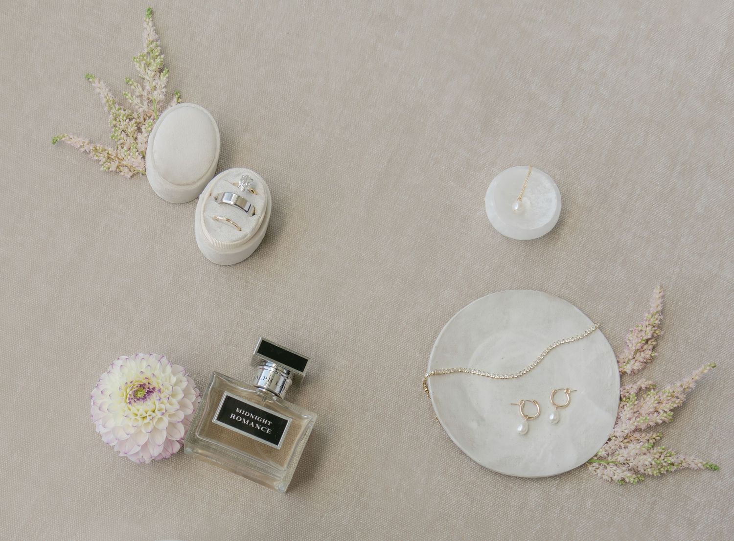 Minimalist flat lay of wedding accessories including perfume bottles and delicate dried flowers on beige background.