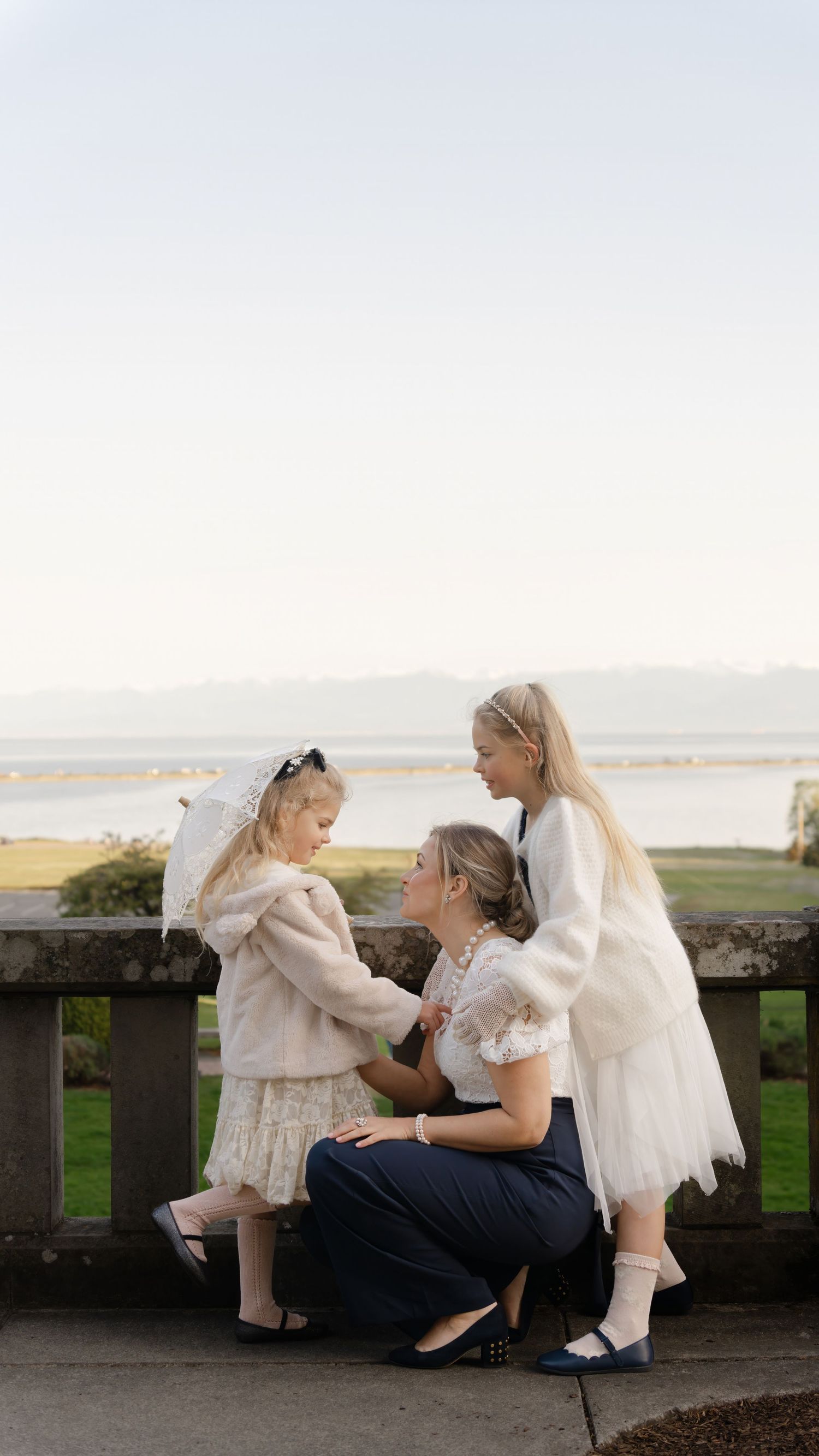 A touching family scene overlooking a waterfront with everyone dressed in white and cream tones.