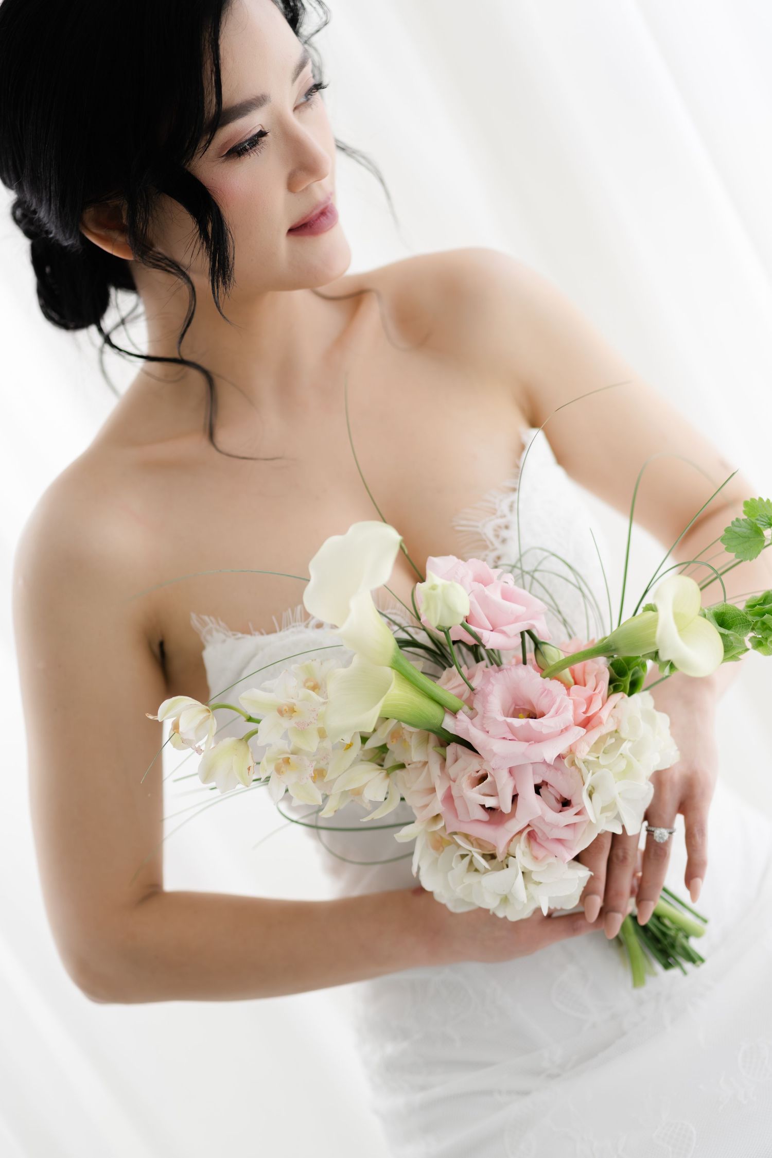 Elegant bride in strapless white lace gown holds a bouquet of pink roses and white calla lilies.