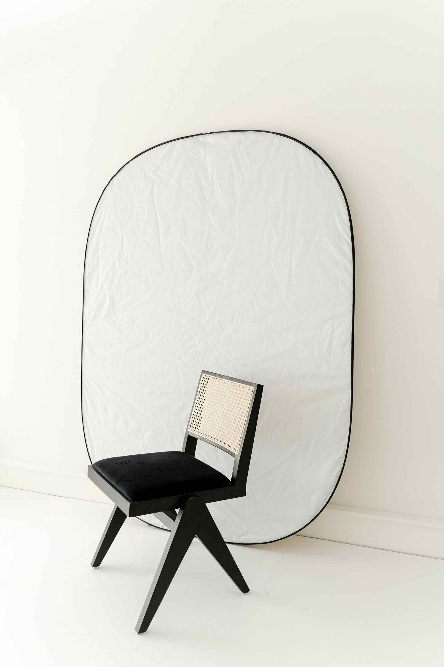 Black contemporary chair positioned in front of large white reflector or backdrop.