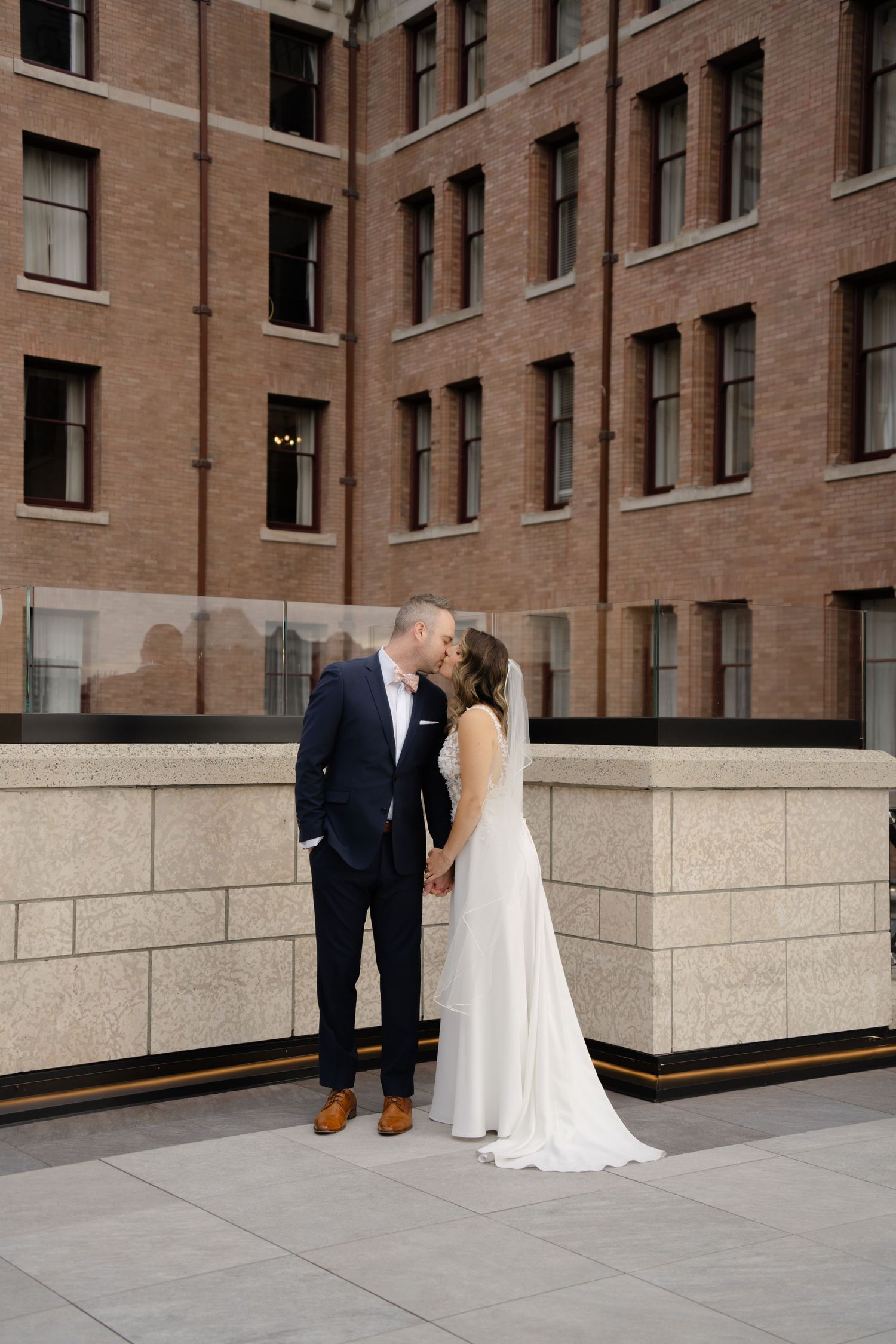 Wedding couple shares intimate moment against brick building facade with stone base.