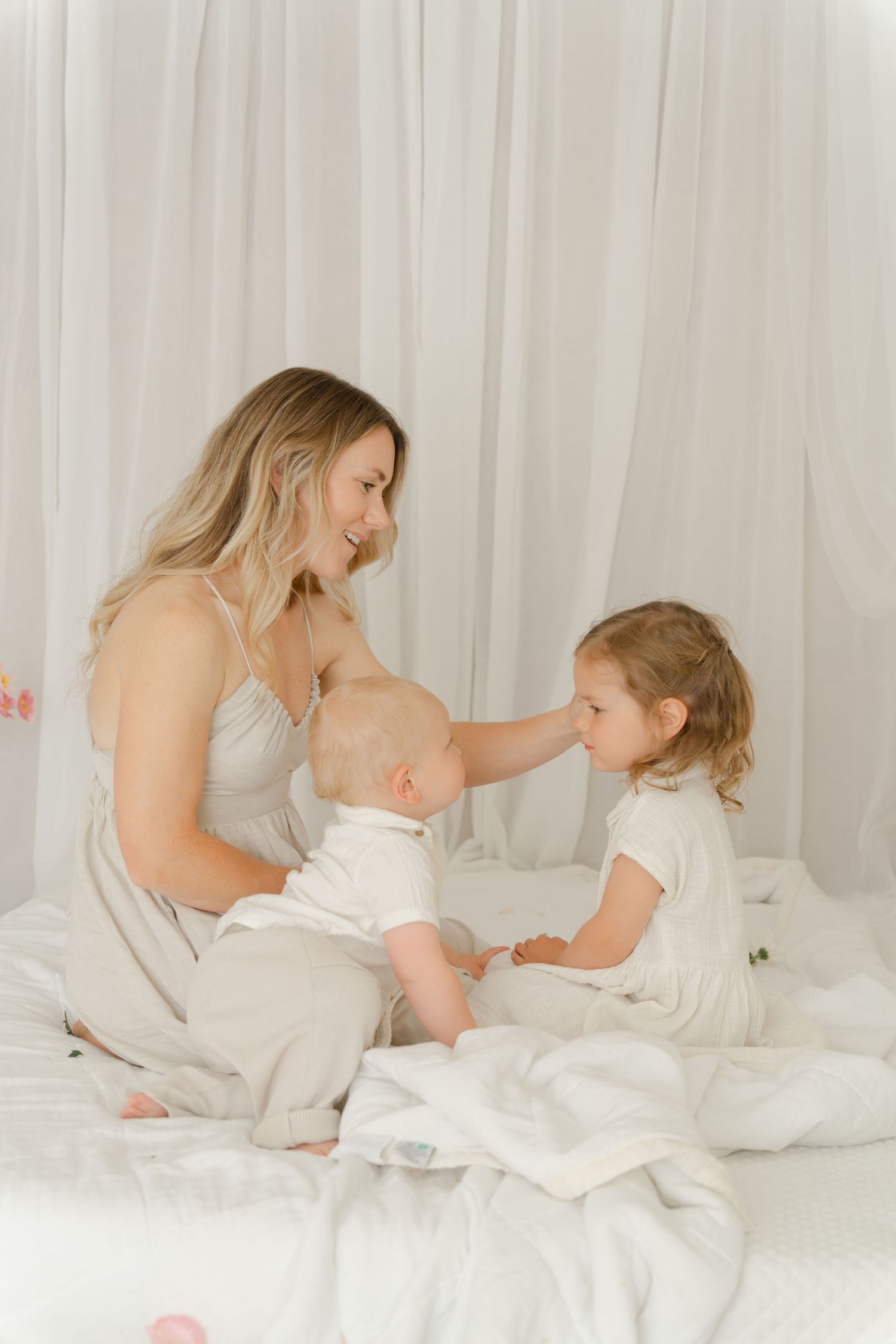 A sweet family scene on white bedding with soft natural lighting from a window.