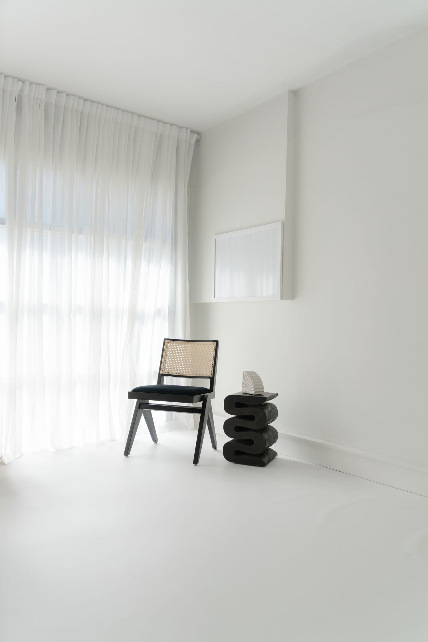 Minimalist white room with black furniture and sheer curtains showcasing contemporary interior design.
