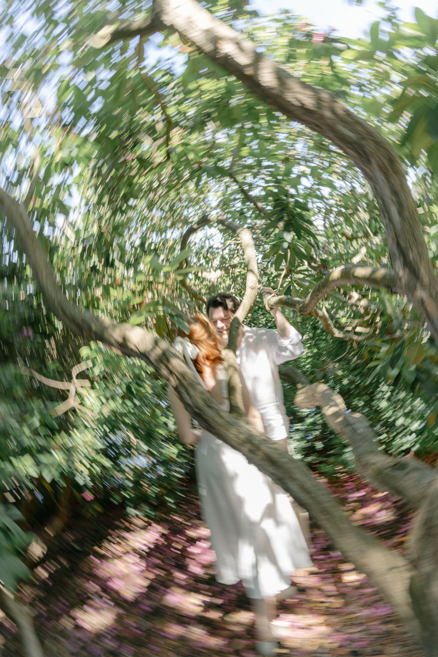 Motion-blurred sequence of a couple in white climbing and playing in a tree surrounded by greenery.