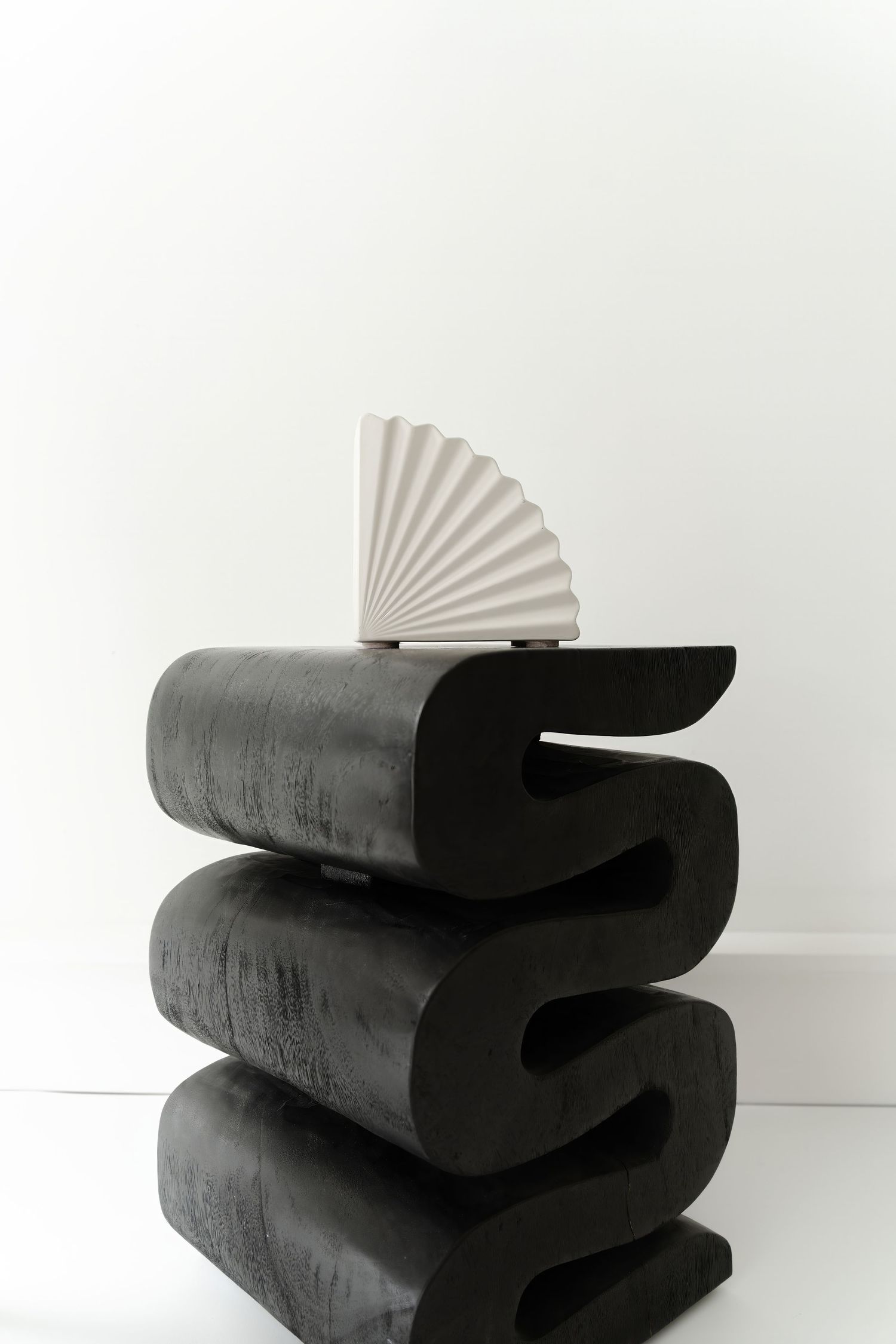 Abstract black sculptural piece with fan-like white element photographed against white background.