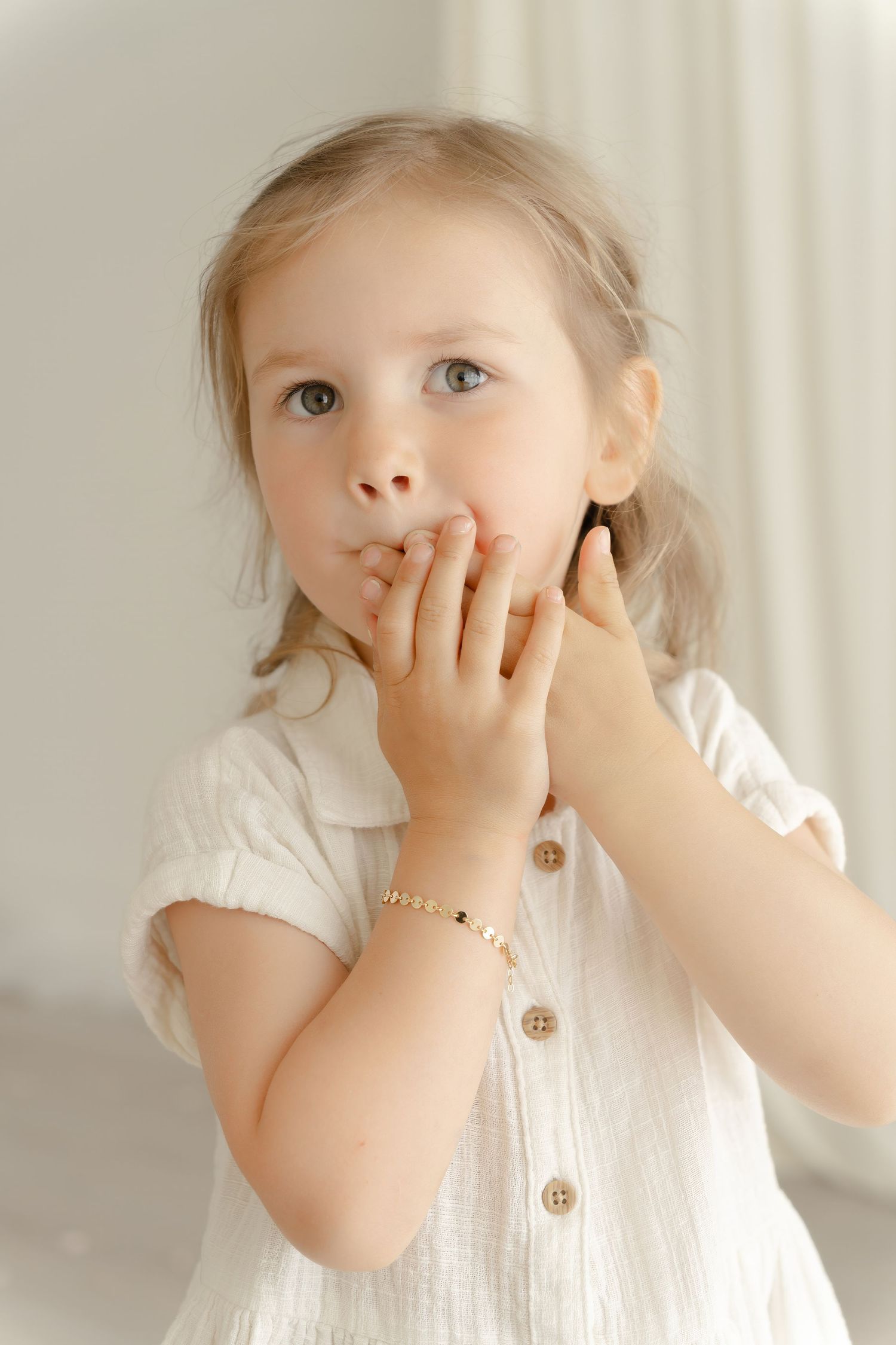 A close-up portrait of a young child in a white button-up dress with delicate jewelry.