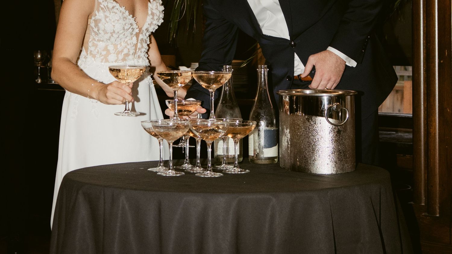 Elegant wedding reception setup with champagne glasses and ice bucket on dark tablecloth.