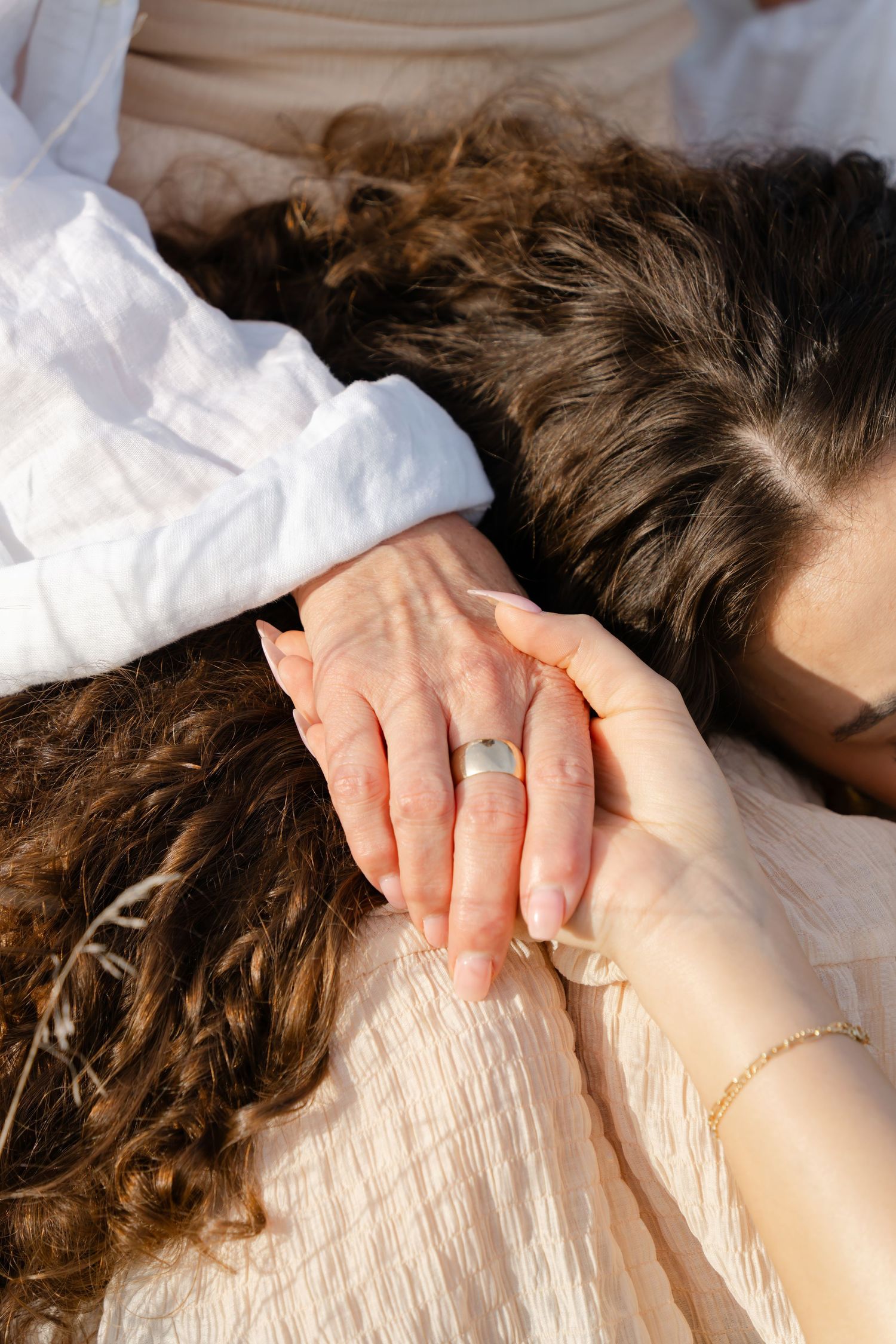 Close-up of hands with rings entwined on white fabric in sunlight.