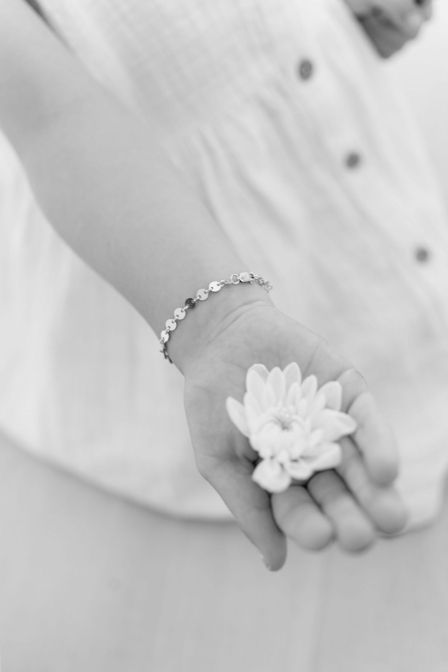 Delicate black and white close-up of hands with jewelry holding small white flowers.