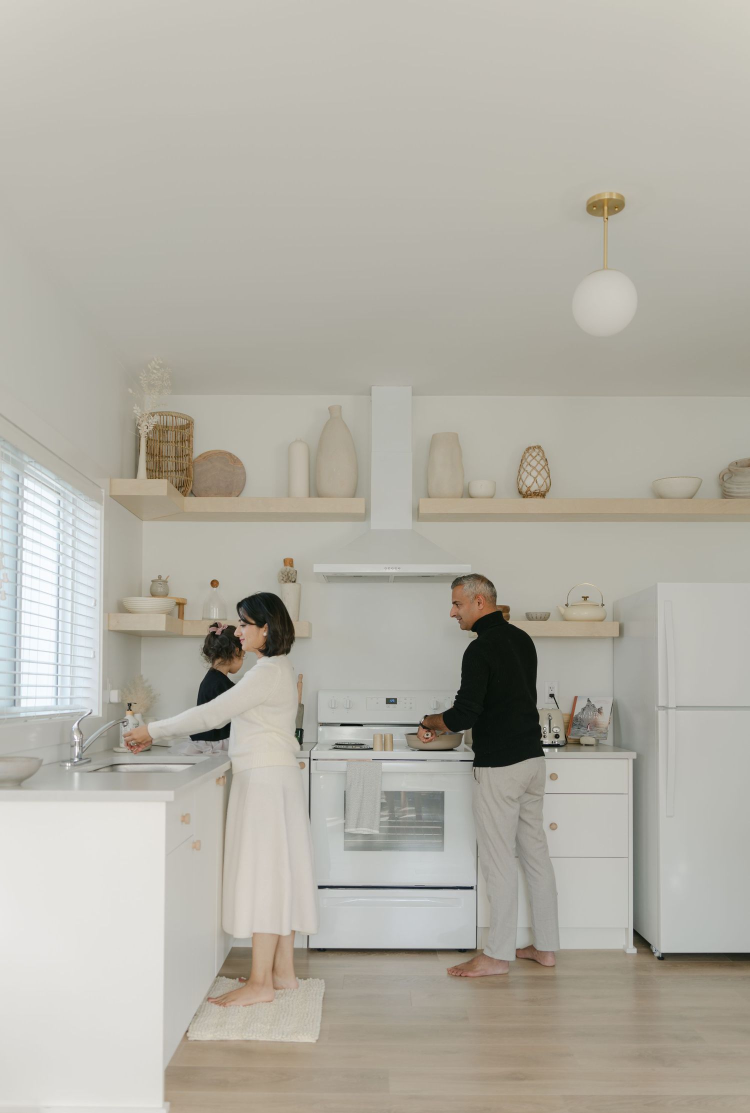 A sequence of five images showing two people cooking together in a minimalist white kitchen with wooden floors.