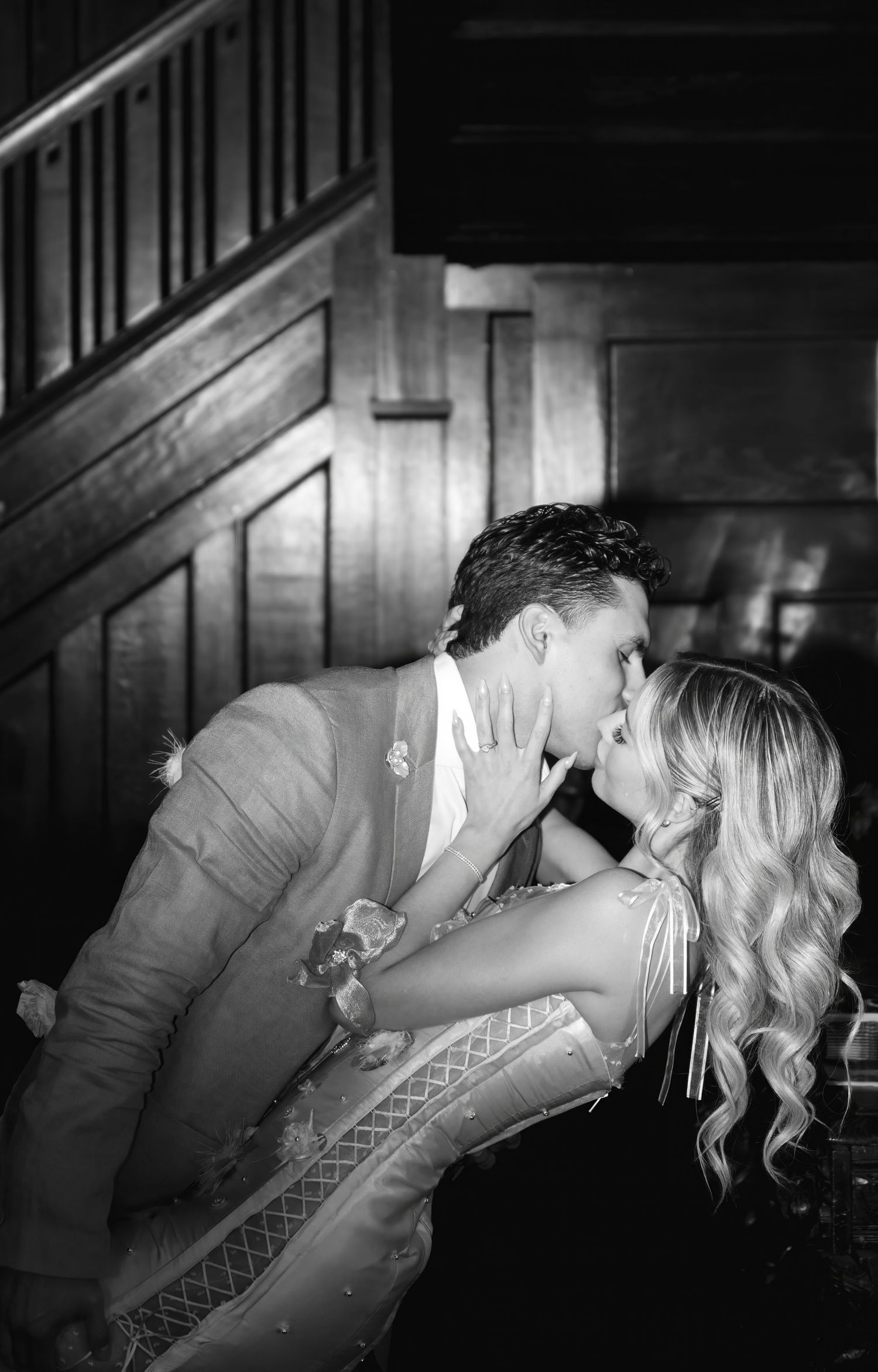 Romantic black and white photo of couple near wooden staircase.