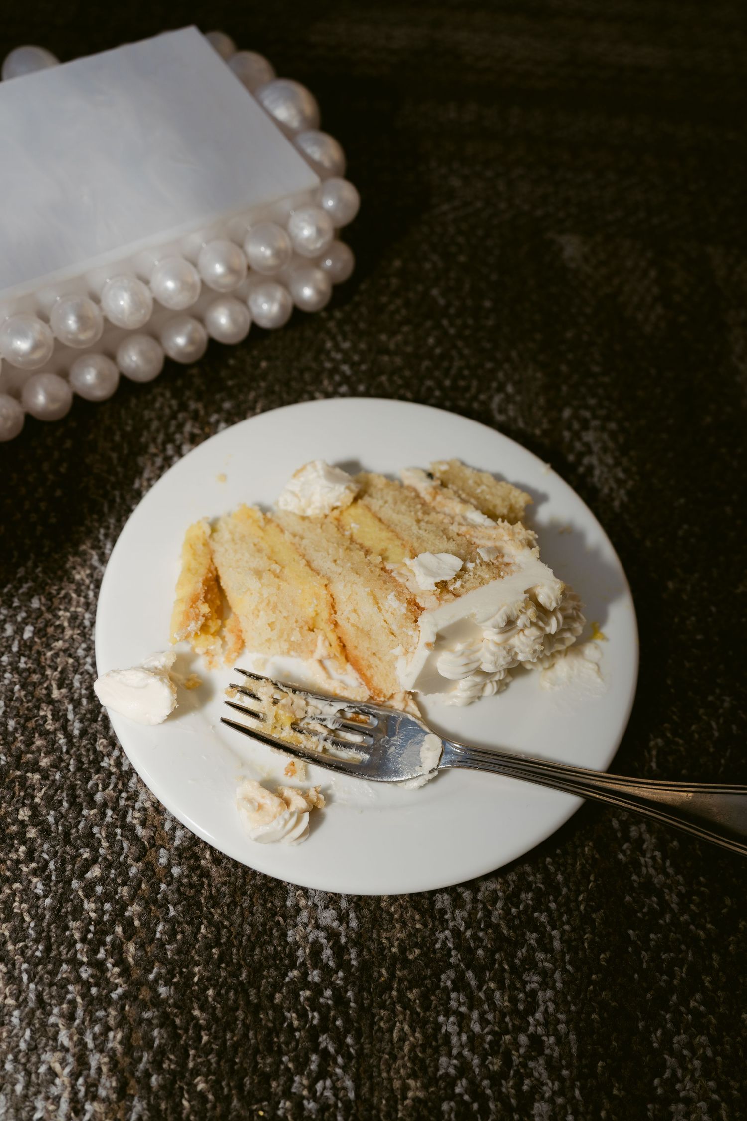 A partially eaten slice of wedding cake with a pearl decoration on a white plate.