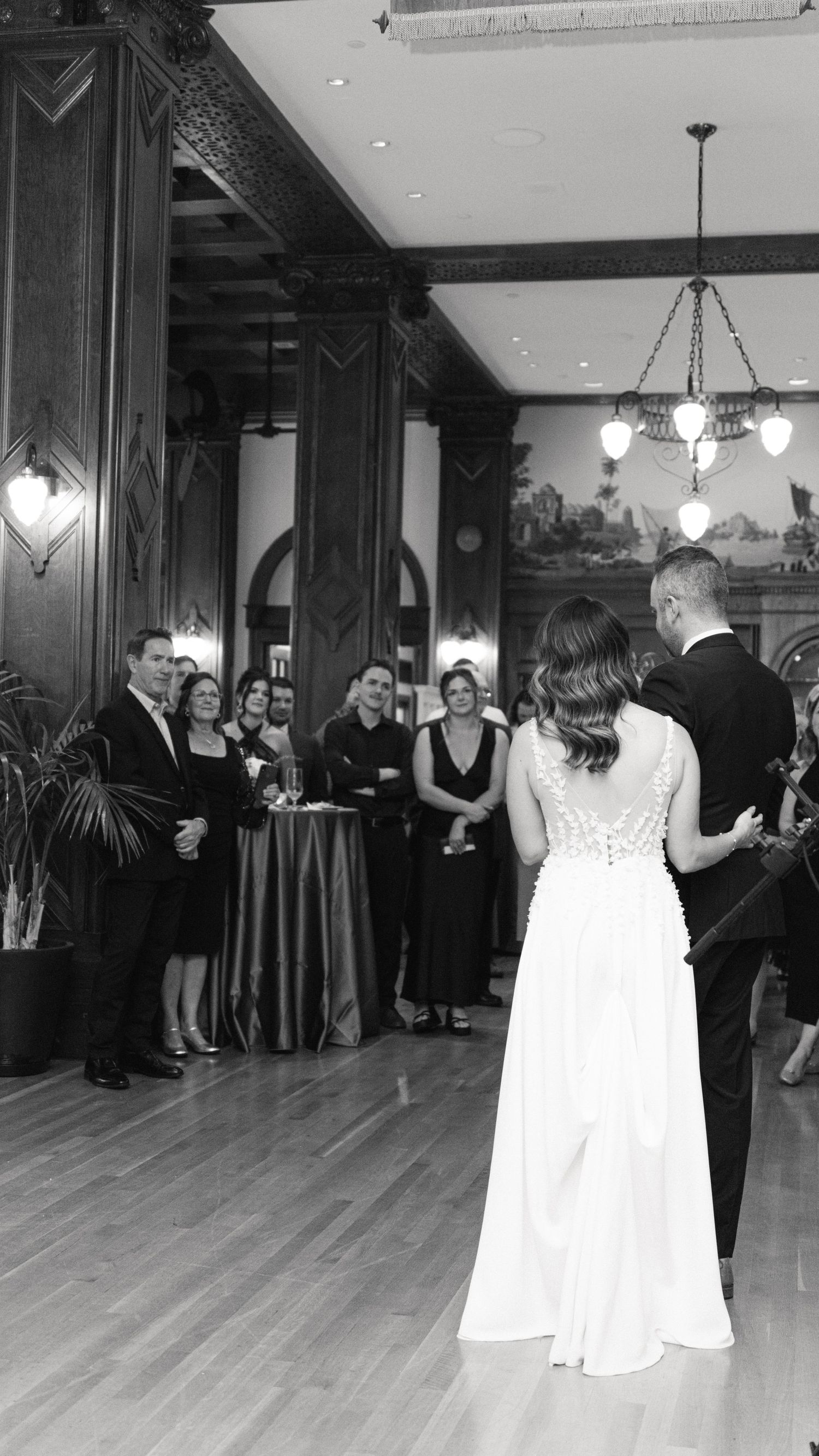 Wedding reception dance in an elegant ballroom with wood floors and chandeliers.