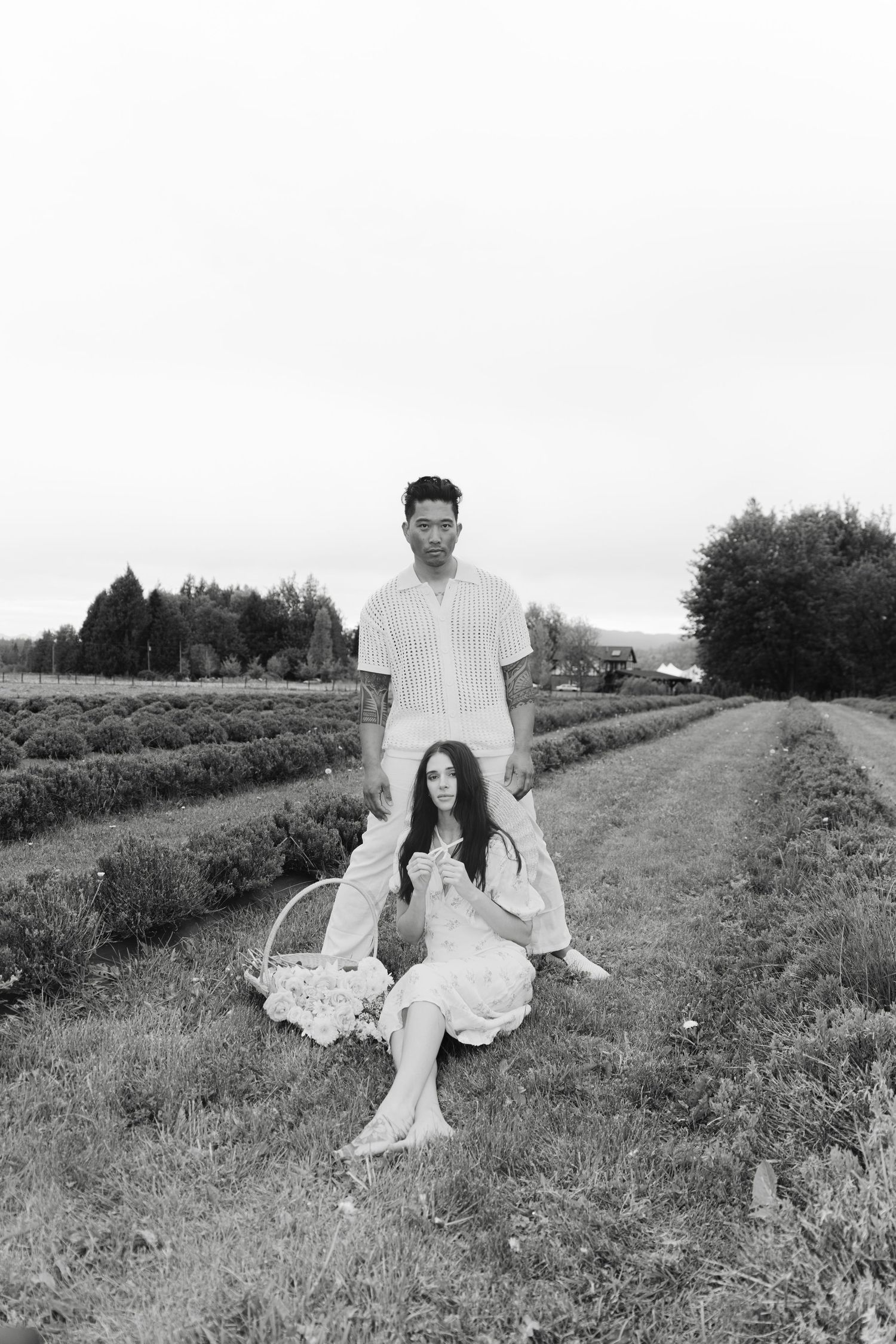 Black and white portrait of a couple relaxing in a grassy field with dramatic sky.
