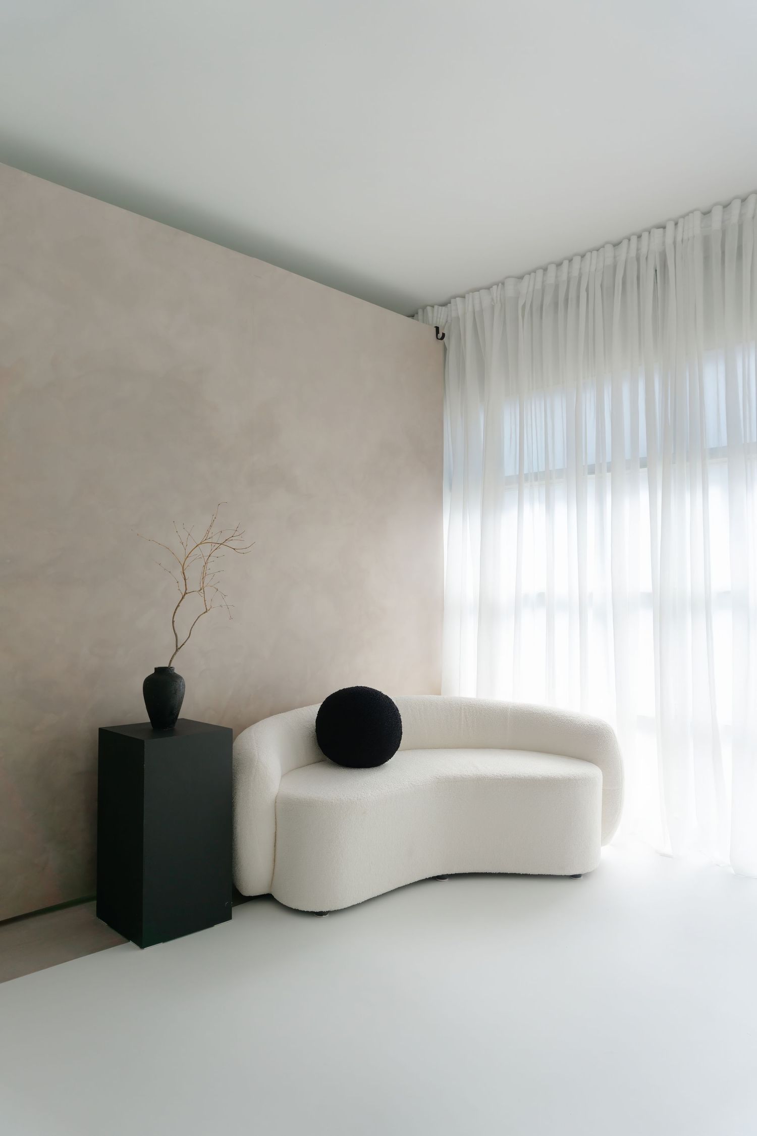 Curved white sofa with modern black accent pieces in bright minimalist room with sheer curtains.