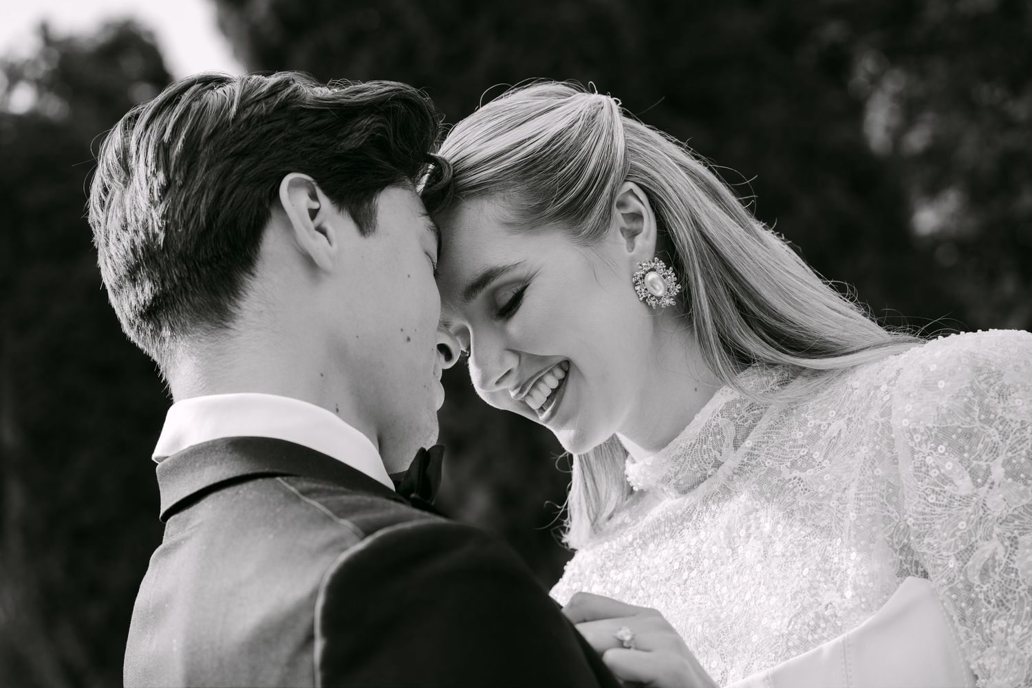 Black and white wedding photo of a smiling bride and groom in formal attire sharing an intimate moment outdoors.