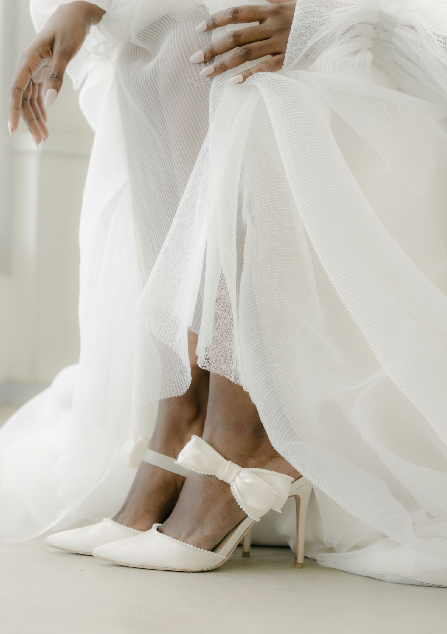 Close-up details of white bridal shoes and dress hem against light background.