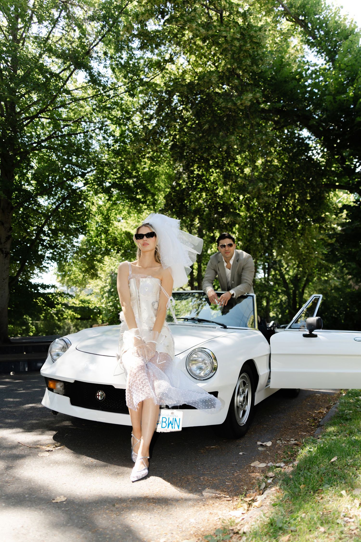 Vintage white sports car parked under shady trees on sunny day.