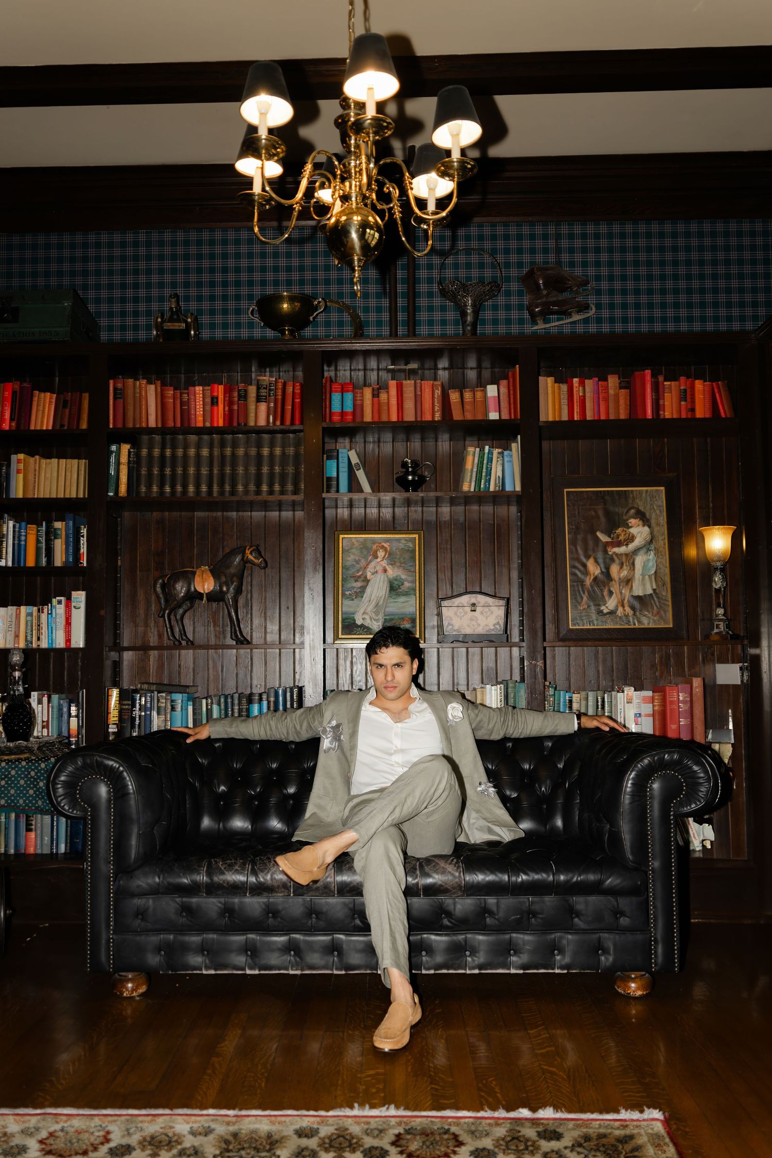 Elegant library setting with leather sofa, brass chandelier, and dark wood bookshelves filled with classic volumes.