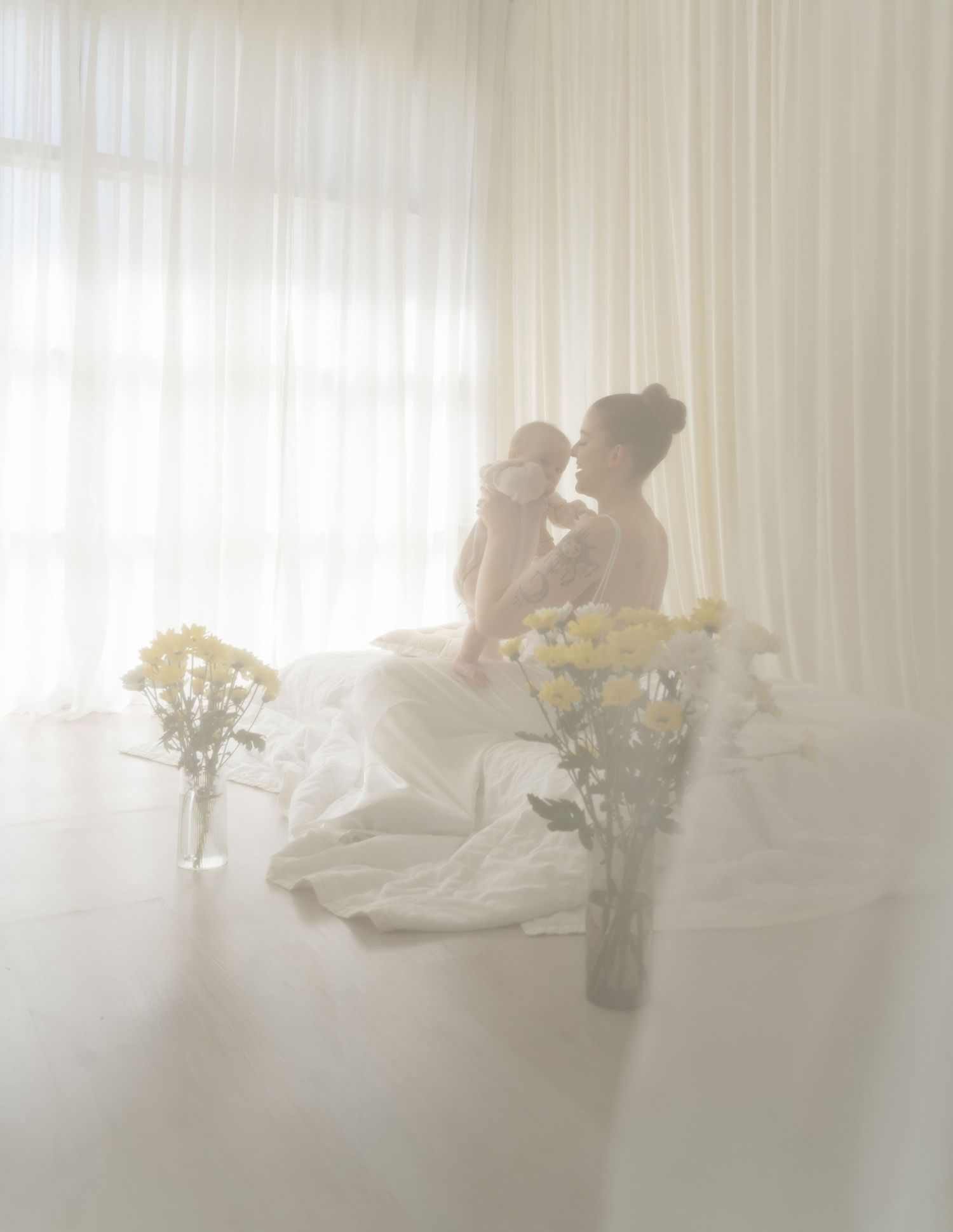 Soft ethereal indoor scene with yellow flowers in vase by sheer white curtains.