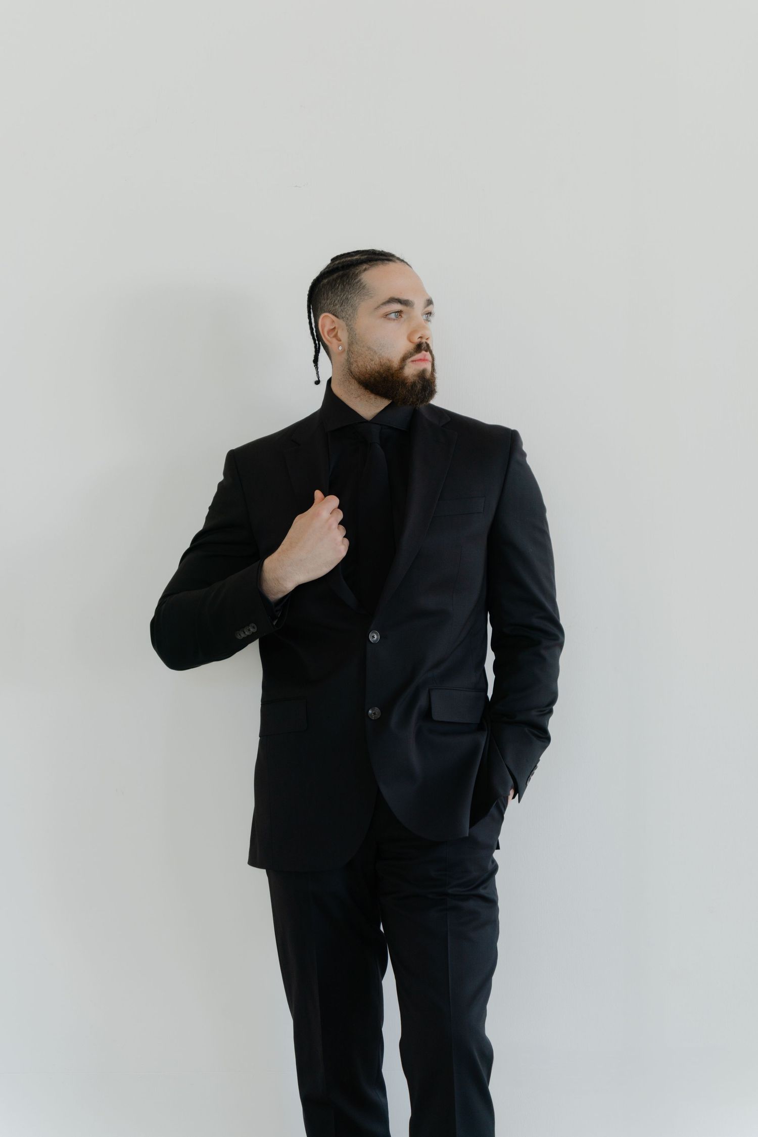 Stylish groom in black suit poses against white background.