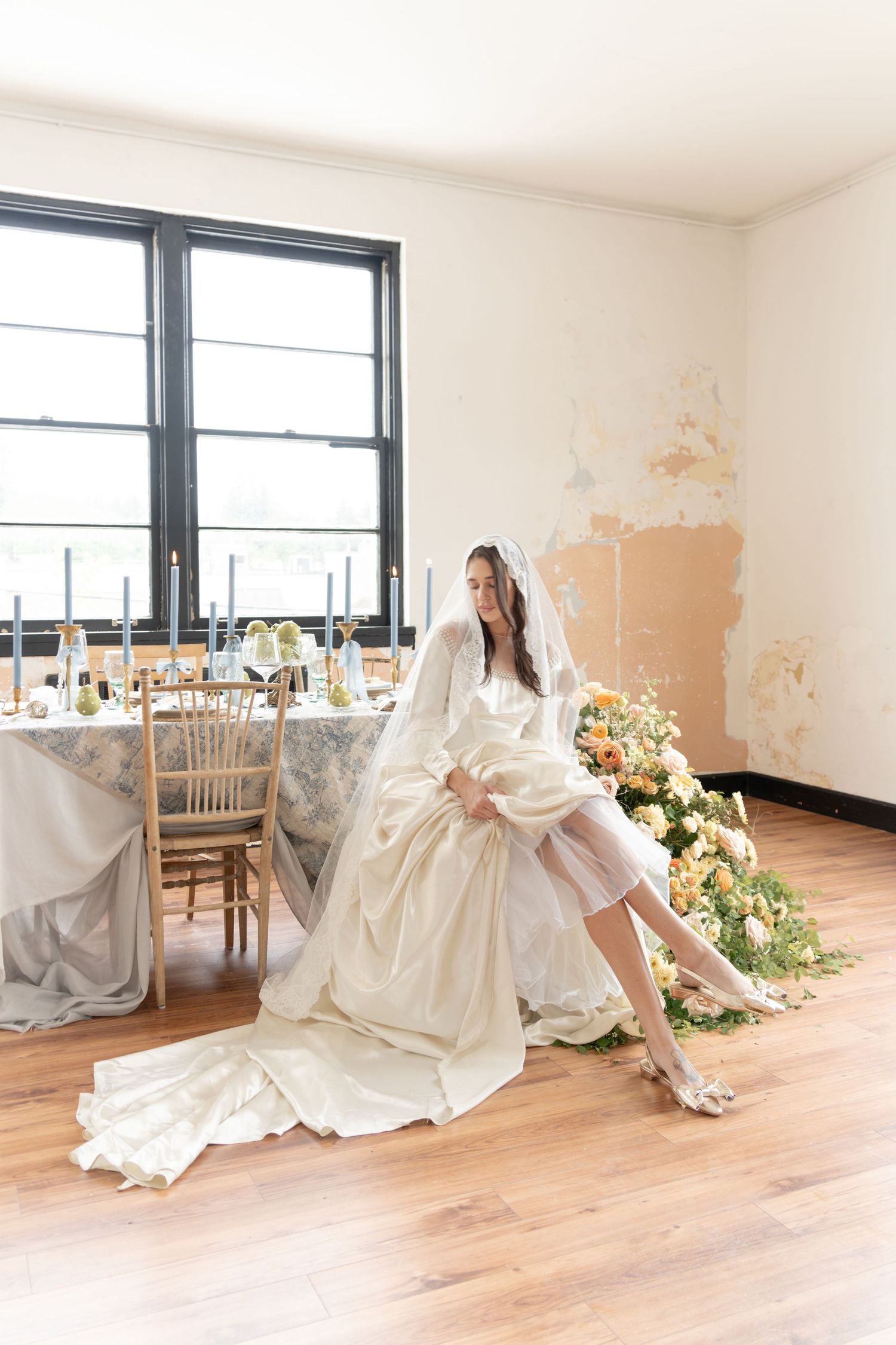 Wedding dress silhouettes in natural light with floral arrangements on hardwood floors.