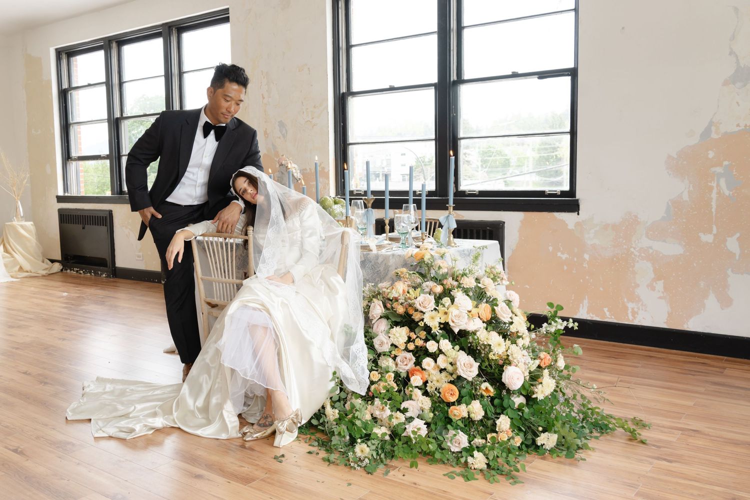 Wedding photoshoot scene with floral arrangements and natural window lighting.
