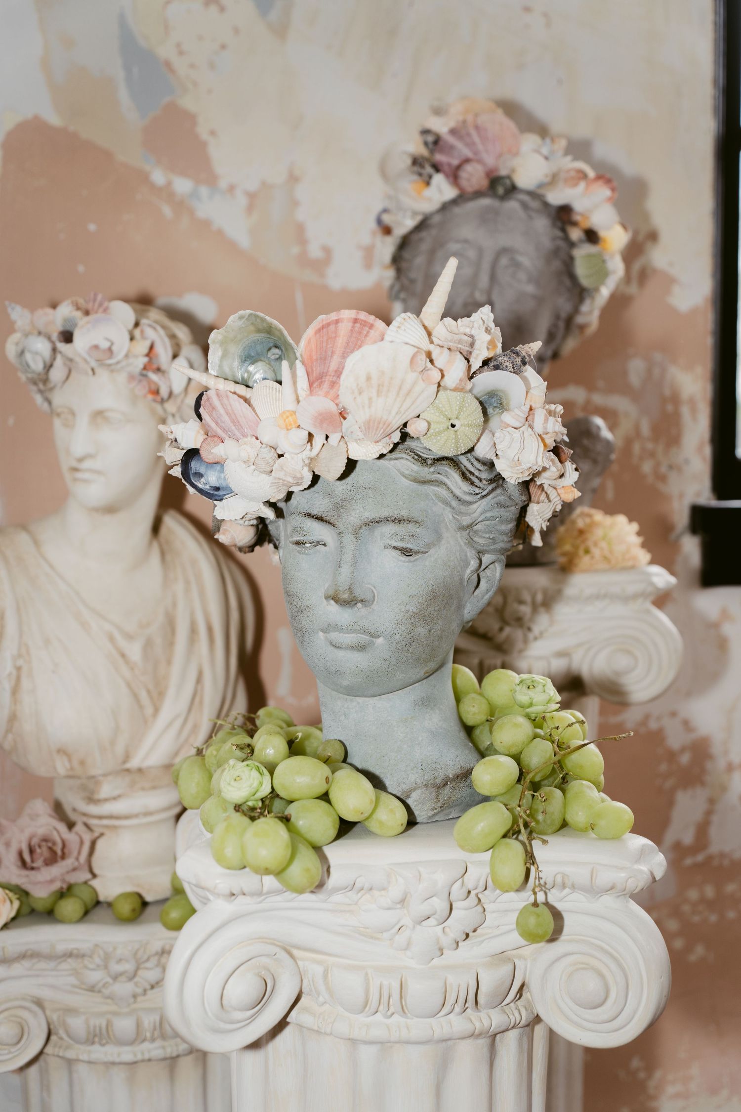 Decorative stone bust adorned with floral crown and grapes on classical column pedestal.