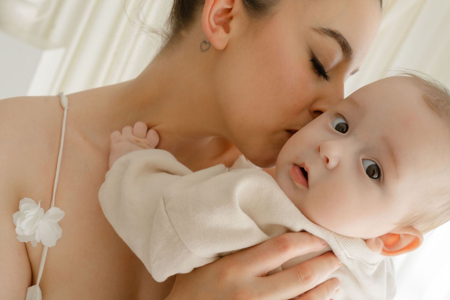 Tender moment captured in soft natural light with white fabric and gentle expressions.