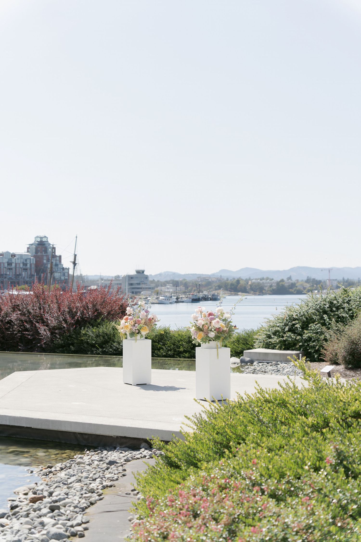 Outdoor wedding setup with white pedestals and floral arrangements overlooking a serene waterway at Inn at Laurel Point Victoria BC