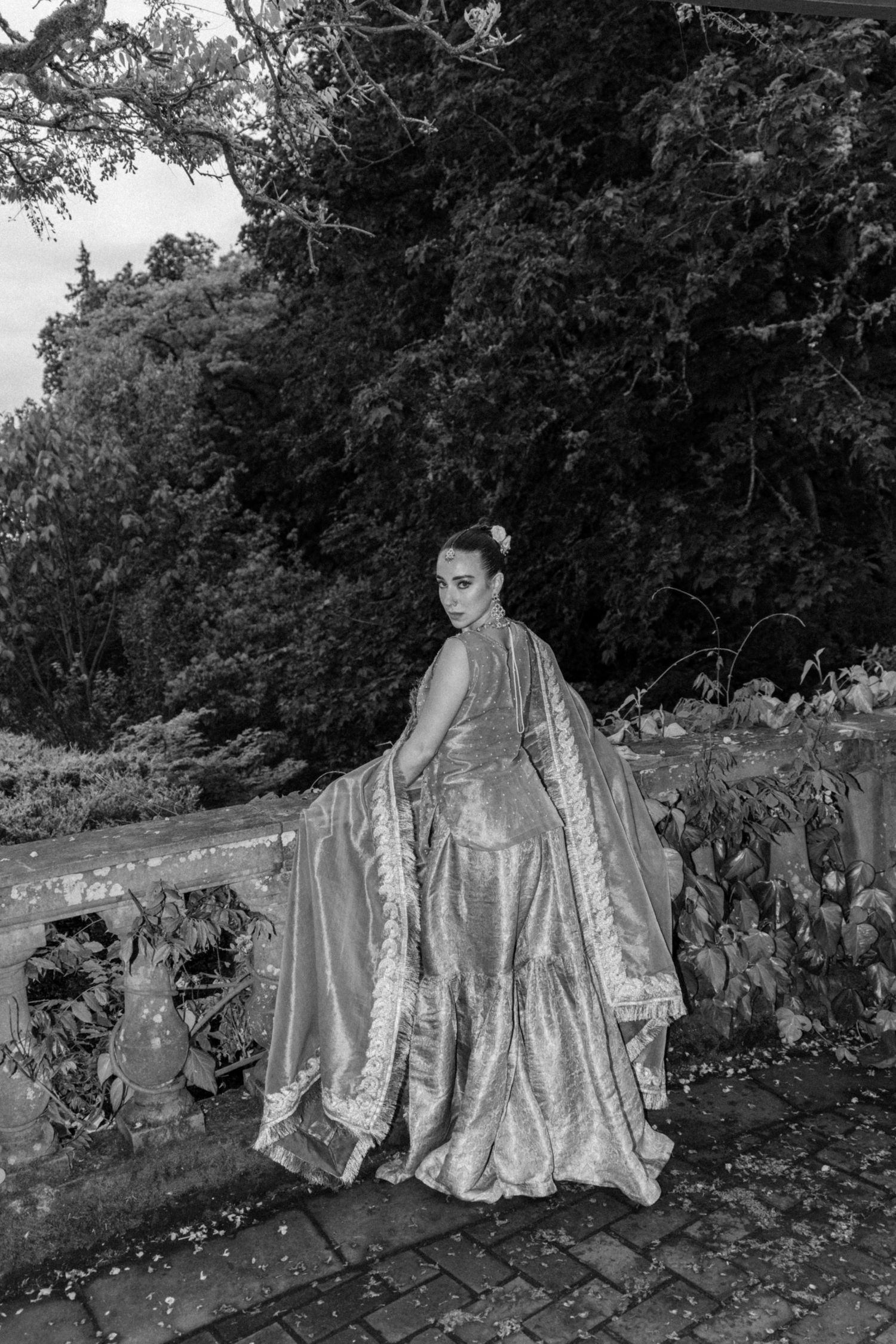Artistic black and white wedding portrait featuring flowing dress fabric in garden setting.