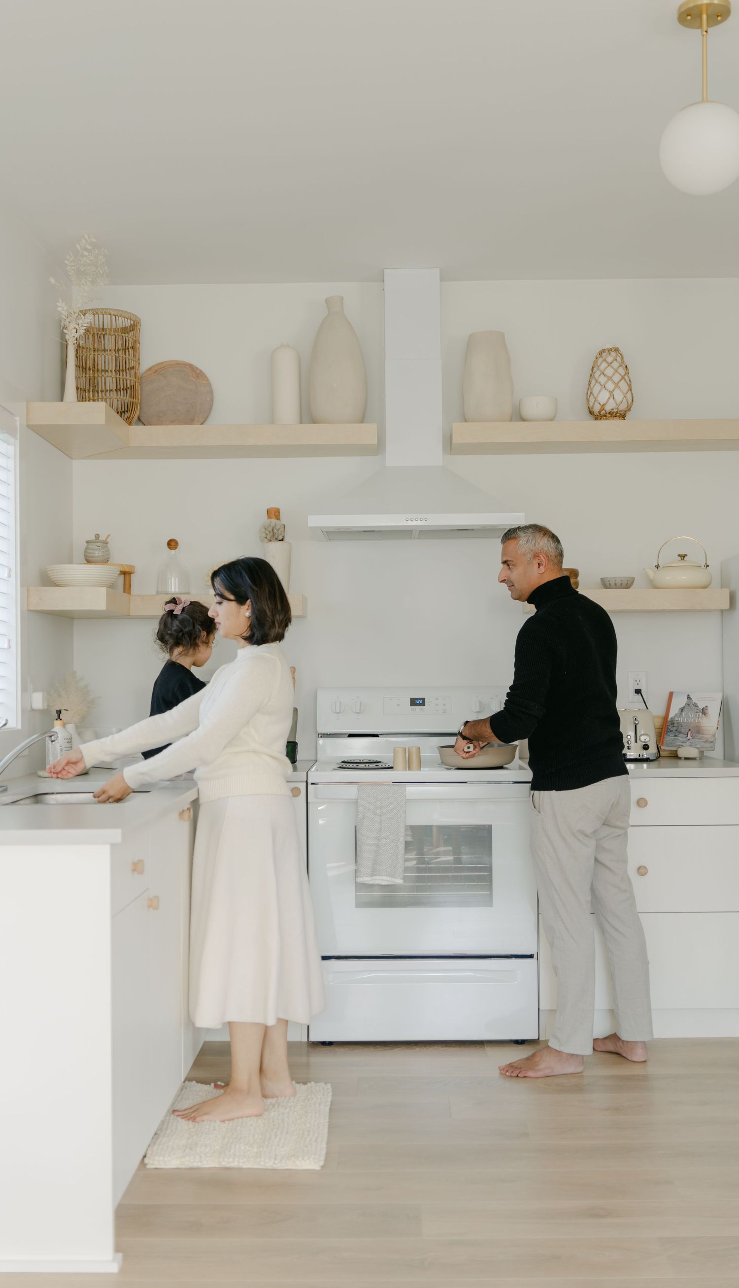Family cooking together in a bright minimalist white kitchen with floating shelves.
