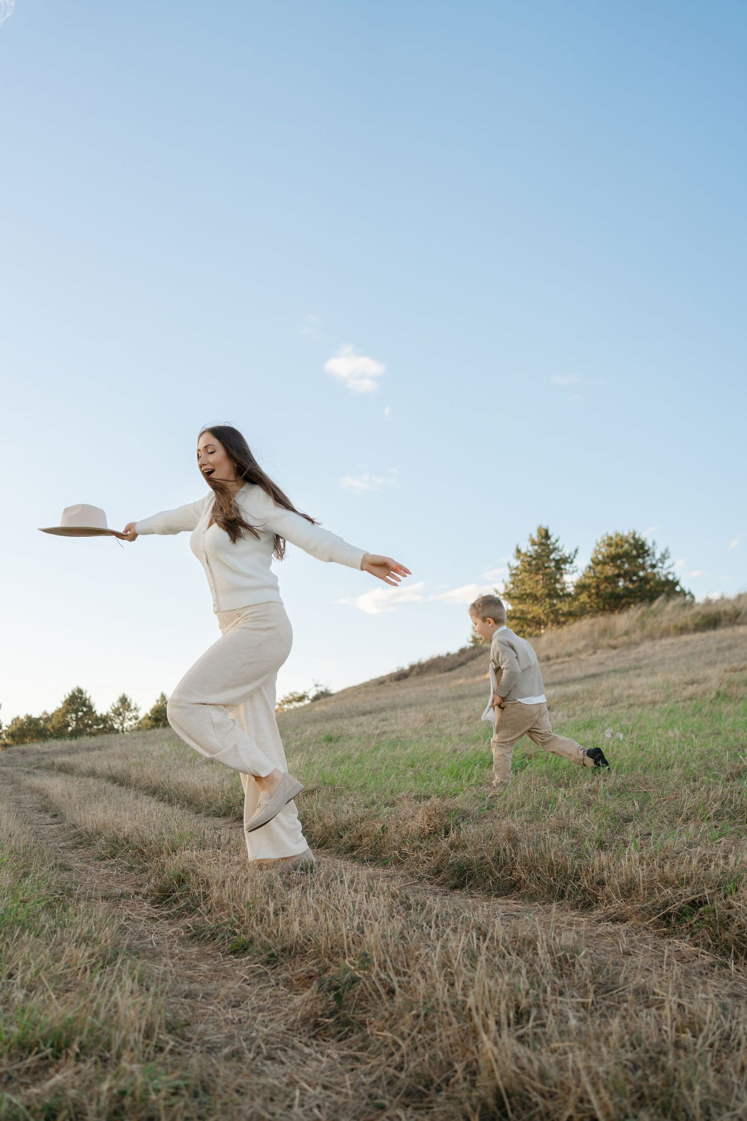 Two people in white outfits joyfully leaping and dancing on a grassy hillside against a bright blue sky with a small cloud.