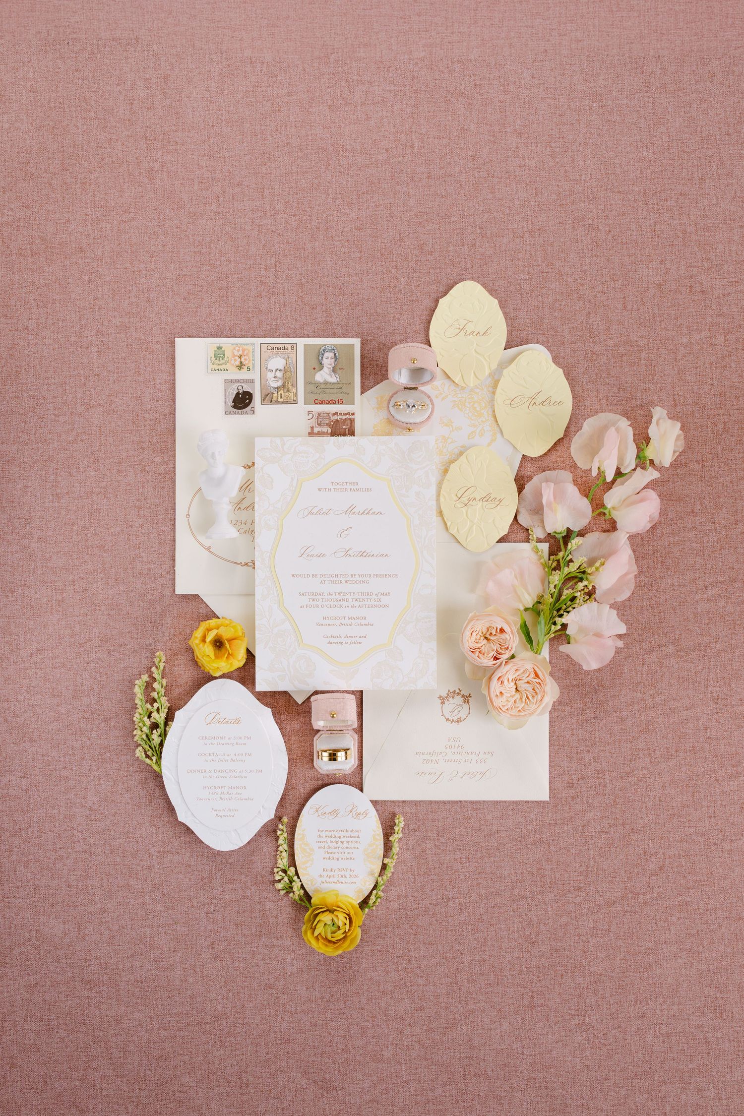 Elegant wedding invitation suite with gold leaf accents, pink roses, and yellow ranunculus on a dusty rose background. Wedding Flatlay