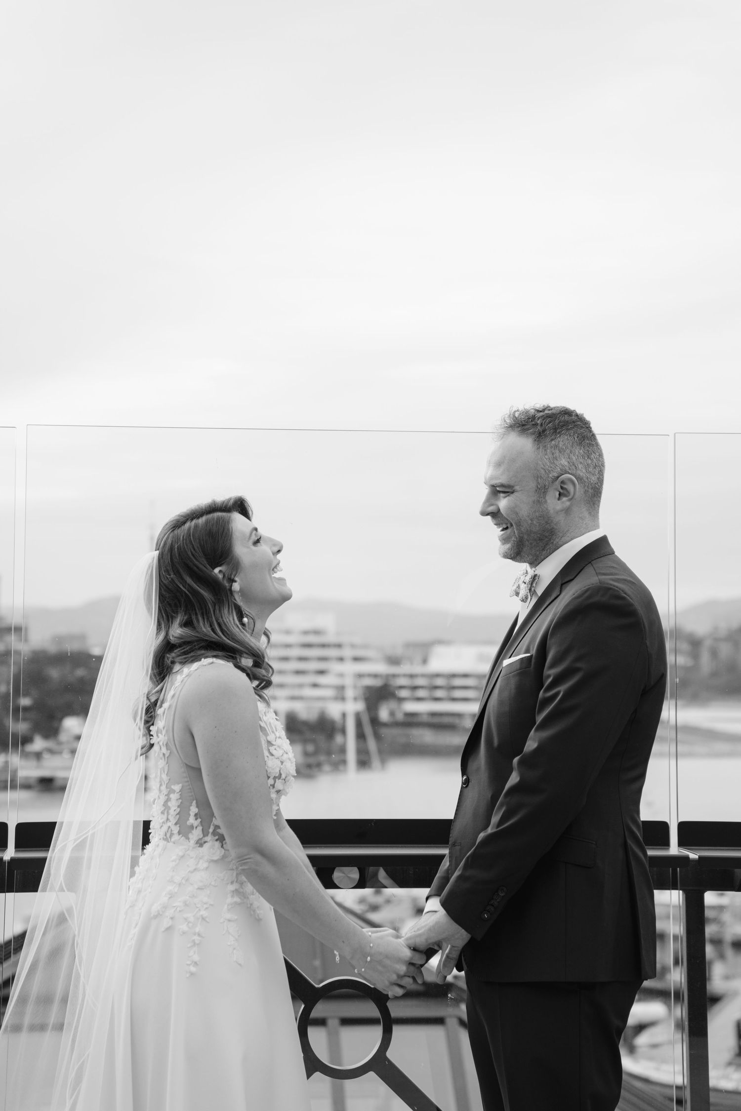 A wedding couple sharing a tender moment on an outdoor terrace overlooking water.
