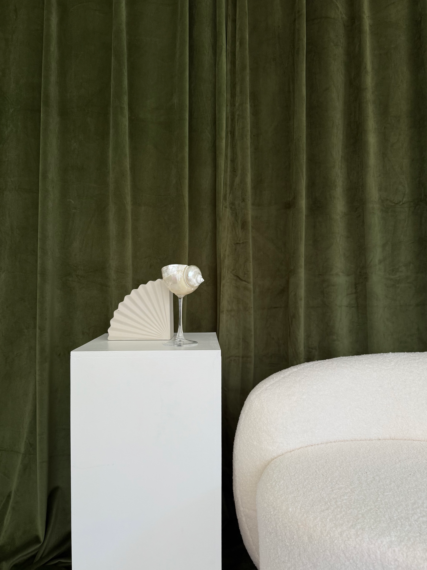 White decorative fan on pedestal against dark green velvet curtain backdrop.