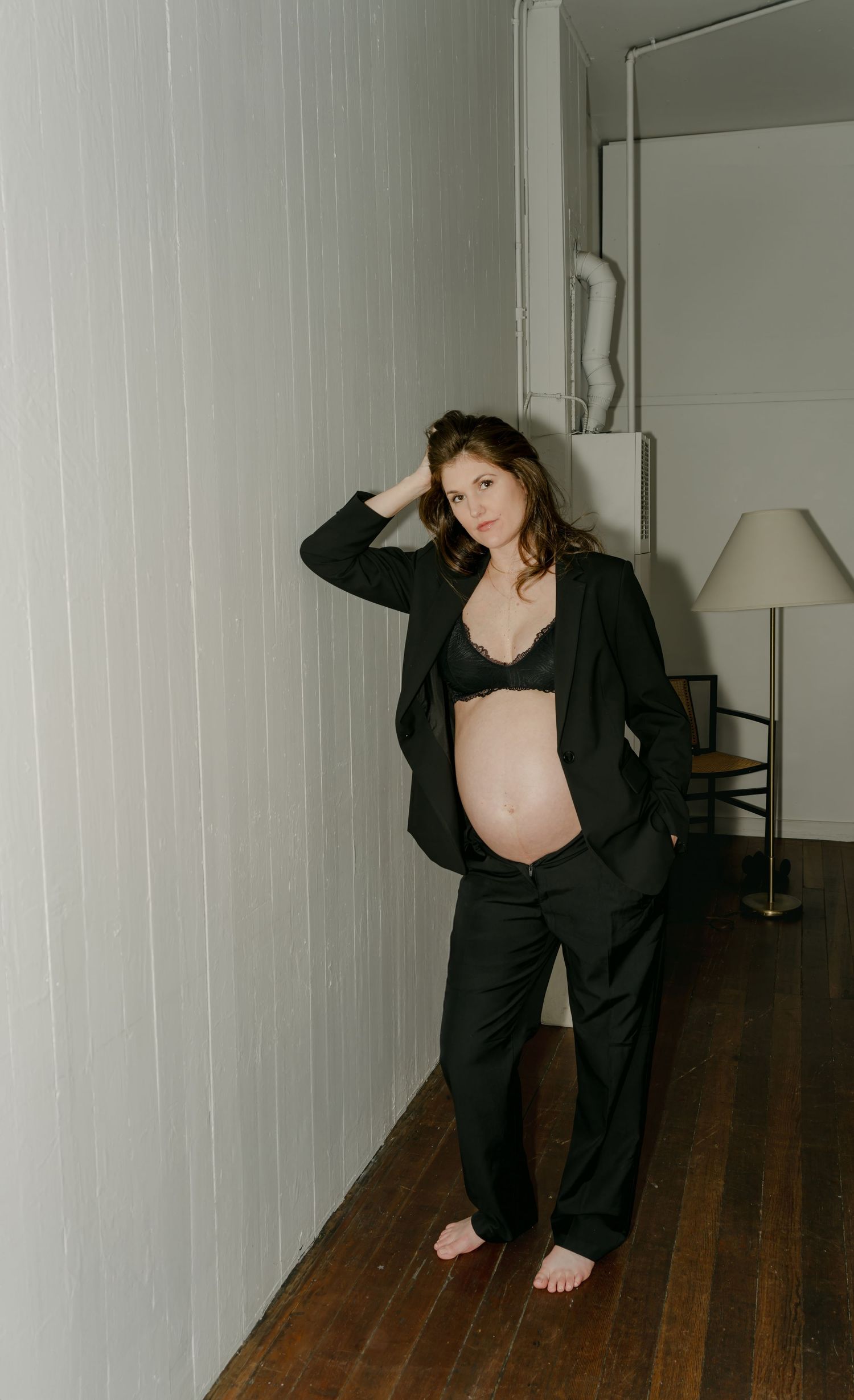 Maternity portrait in black outfit against white wall with wooden floors.
