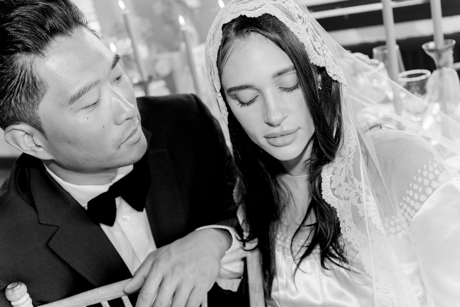 Black and white photo of a groom in tuxedo and bride in lace veil sharing an intimate moment at their wedding.